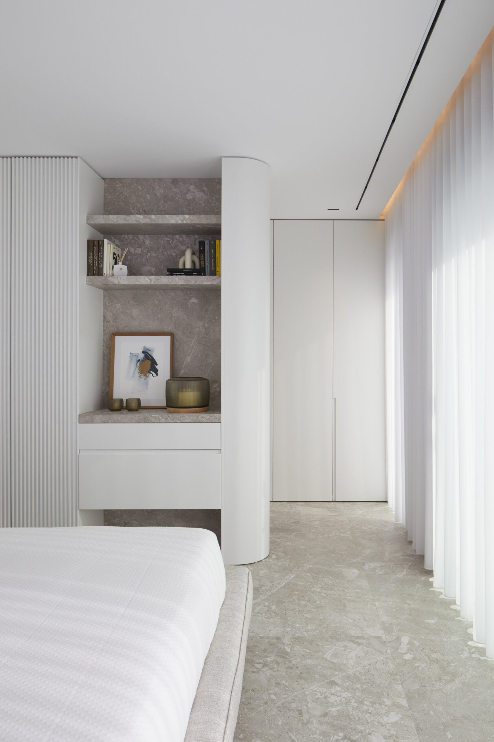 Custom built-ins combine utility and softness. Open shelves hold curated books and objects, while curves, stone, and ribbed details echo the room’s calm, crafted aesthetic.