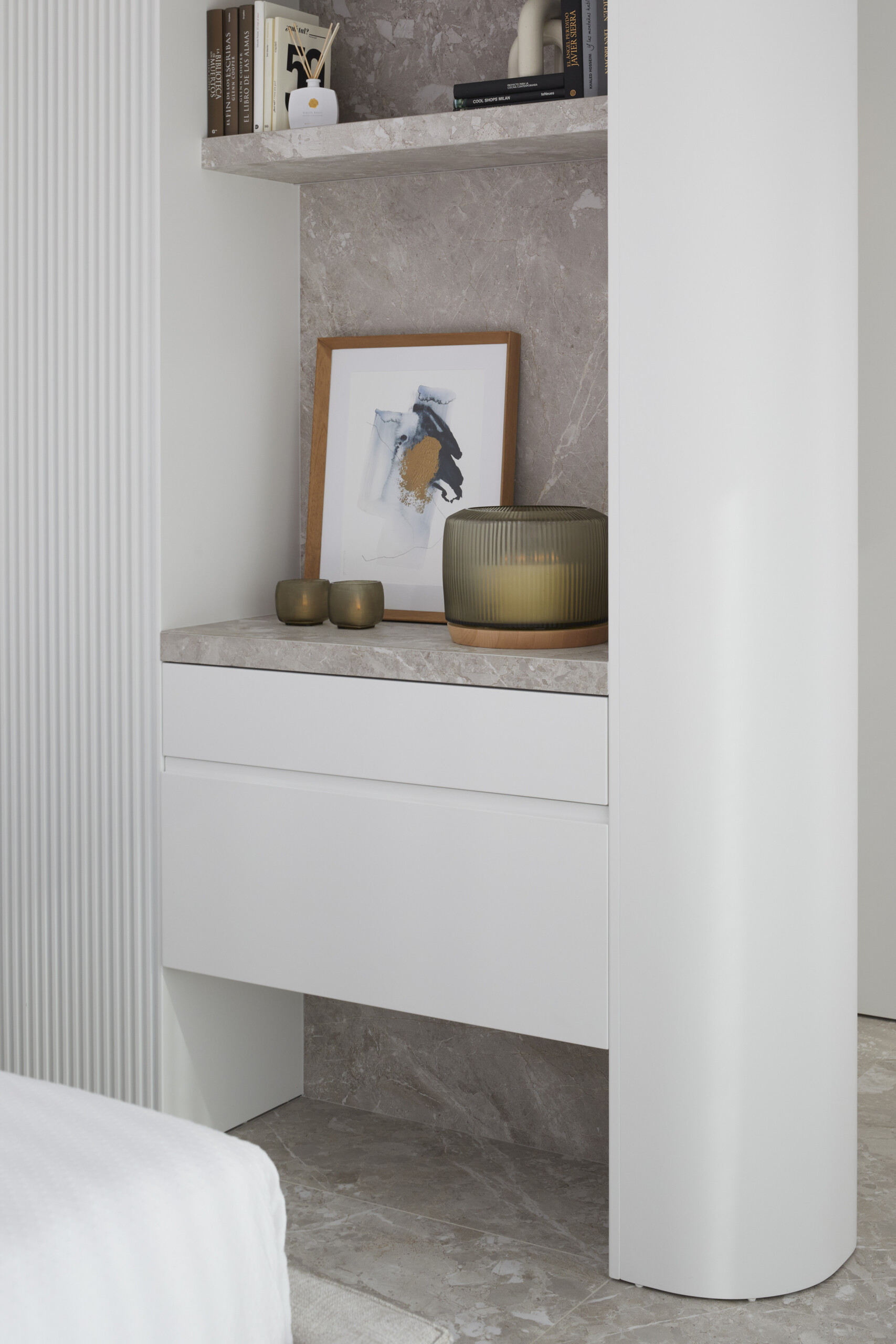 Custom built-ins combine utility and softness. Open shelves hold curated books and objects, while curves, stone, and ribbed details echo the room’s calm, crafted aesthetic.