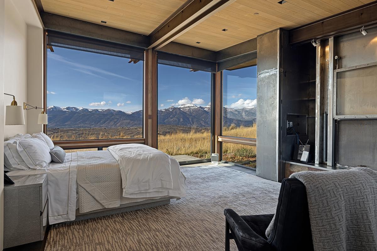 Waking up in this bedroom must feel like stepping into a postcard. Floor-to-ceiling windows wrap the corner, framing golden grasses and snow-capped peaks like a living work of art. The crisp white bedding and soft textures keep things serene and airy, while touches of brushed brass and exposed steel lend a modern edge. Natural light floods the room, shifting throughout the day and making it a perfect retreat for slow mornings, afternoon reads, or stargazing from bed.