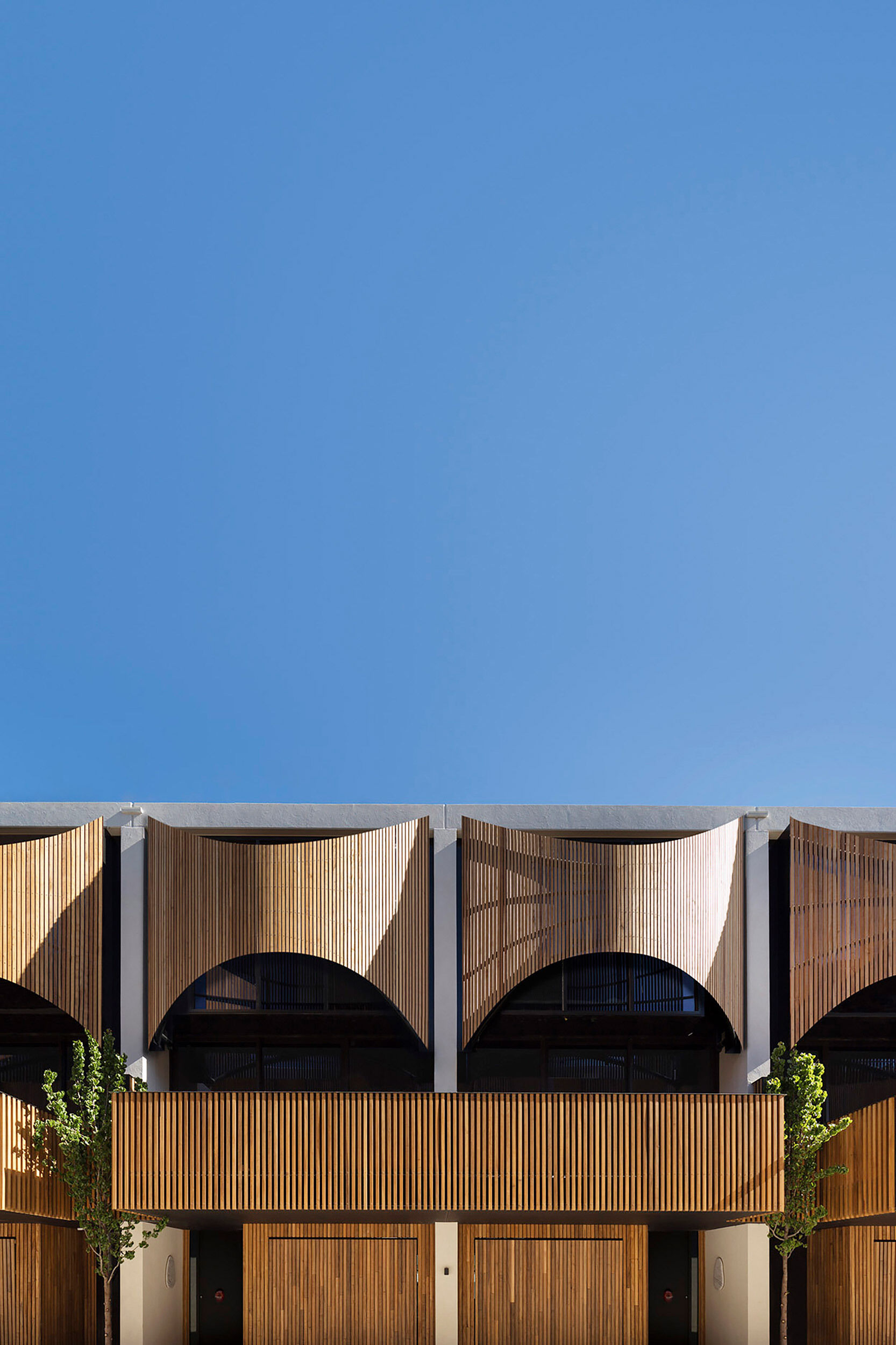 Along a tree-lined shared path, these townhouses feature softly fluted timber screens, overhanging terraces, and a warm, finely detailed palette that adds intimacy and rhythm to the streetscape.