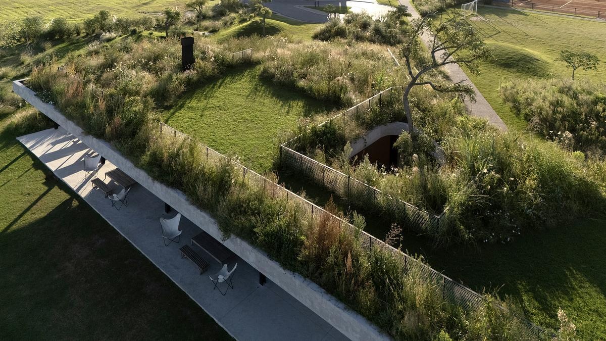 One of this project’s most striking features is its planted roof, which functions as both landscape and architecture. Instead of sitting on top of the building like an accessory, the green roof is woven into the terrain, folding down to meet the ground in a walkable ramp. This design move dissolves the boundary between natural and built, and subtly encourages people to interact with the space in ways that feel intuitive and playful.