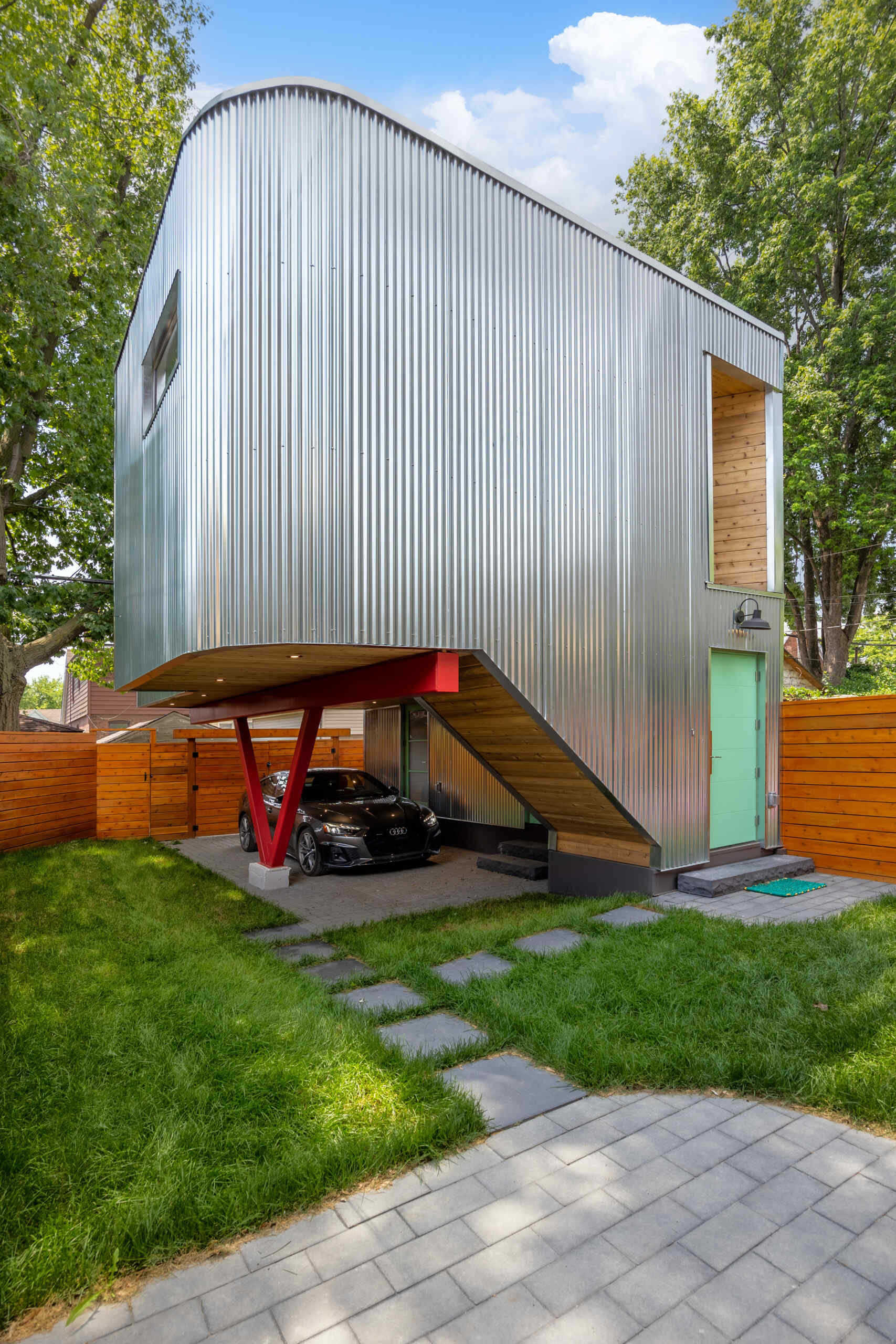This modern laneway house, clad in corrugated metal, is also grounded in warmth. The underside of the carport is clad in cedar, and bursts of vivid accent color appear throughout the structure. These color choices reflect the clients’ affection for folk art and bring a touch of whimsy to the silvery industrial palette above.