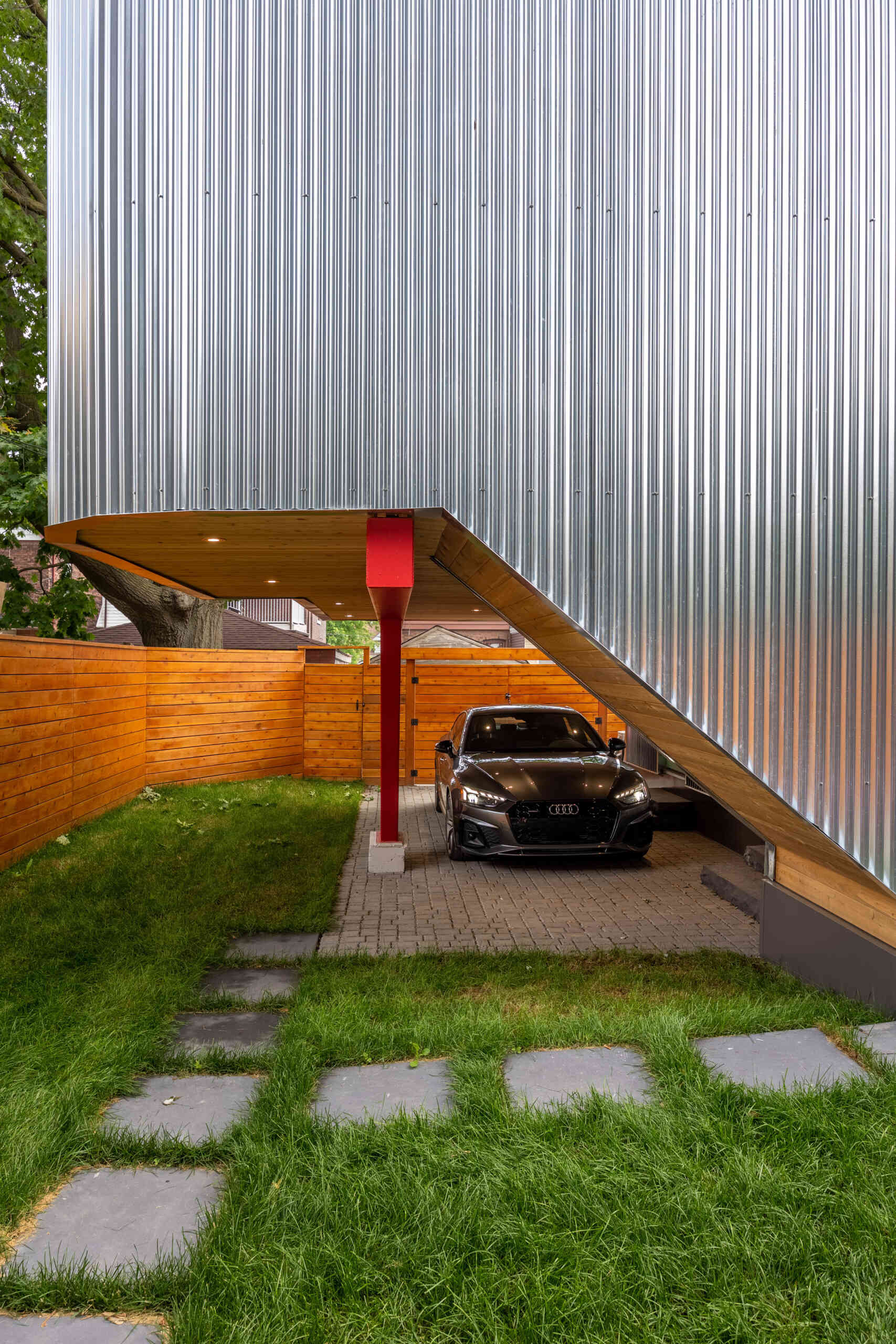 This modern laneway house, clad in corrugated metal, is also grounded in warmth. The underside of the carport is clad in cedar, and bursts of vivid accent color appear throughout the structure. These color choices reflect the clients’ affection for folk art and bring a touch of whimsy to the silvery industrial palette above.