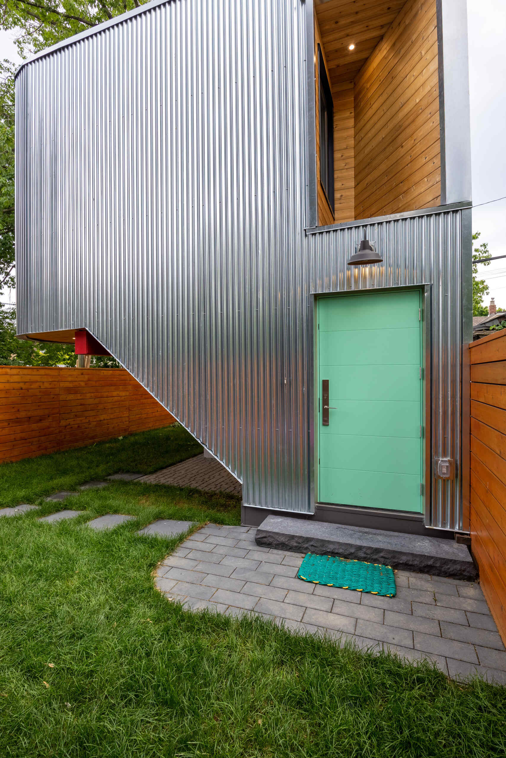 This modern laneway house, clad in corrugated metal, is also grounded in warmth. The underside of the carport is clad in cedar, and bursts of vivid accent color appear throughout the structure. These color choices reflect the clients’ affection for folk art and bring a touch of whimsy to the silvery industrial palette above.