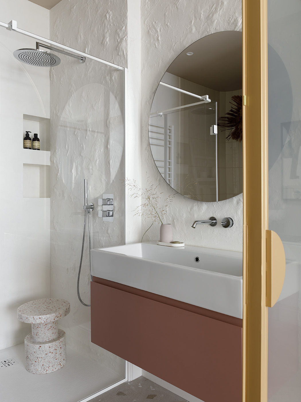 A pair of arched glass doors framed in brushed gold instantly elevate this ensuite bathroom, turning a simple transition into a quiet statement. Textured walls have been paired with a terracotta vanity, bringing just a touch of grounded color.
