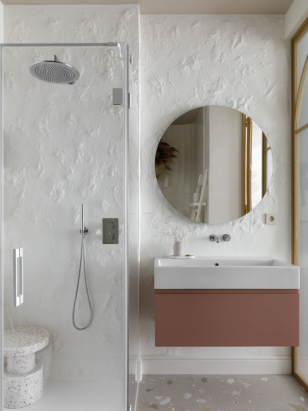A pair of arched glass doors framed in brushed gold instantly elevate this ensuite bathroom, turning a simple transition into a quiet statement. Textured walls have been paired with a terracotta vanity, bringing just a touch of grounded color.