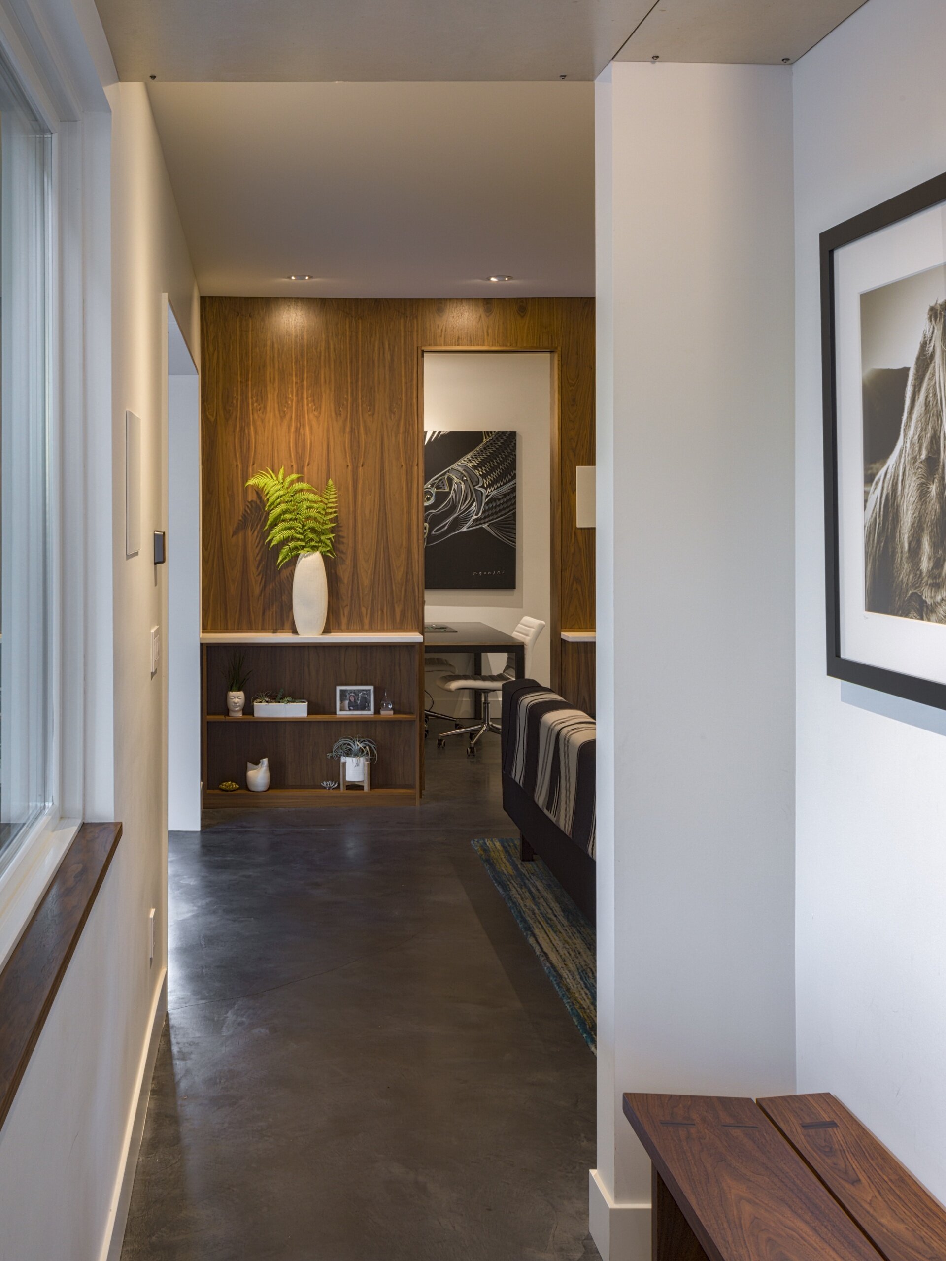 The hallway is simple and efficient, defined by polished concrete floors and white walls that reflect natural light from a side window. Warm wood accents break up the palette, adding texture and contrast without distraction.