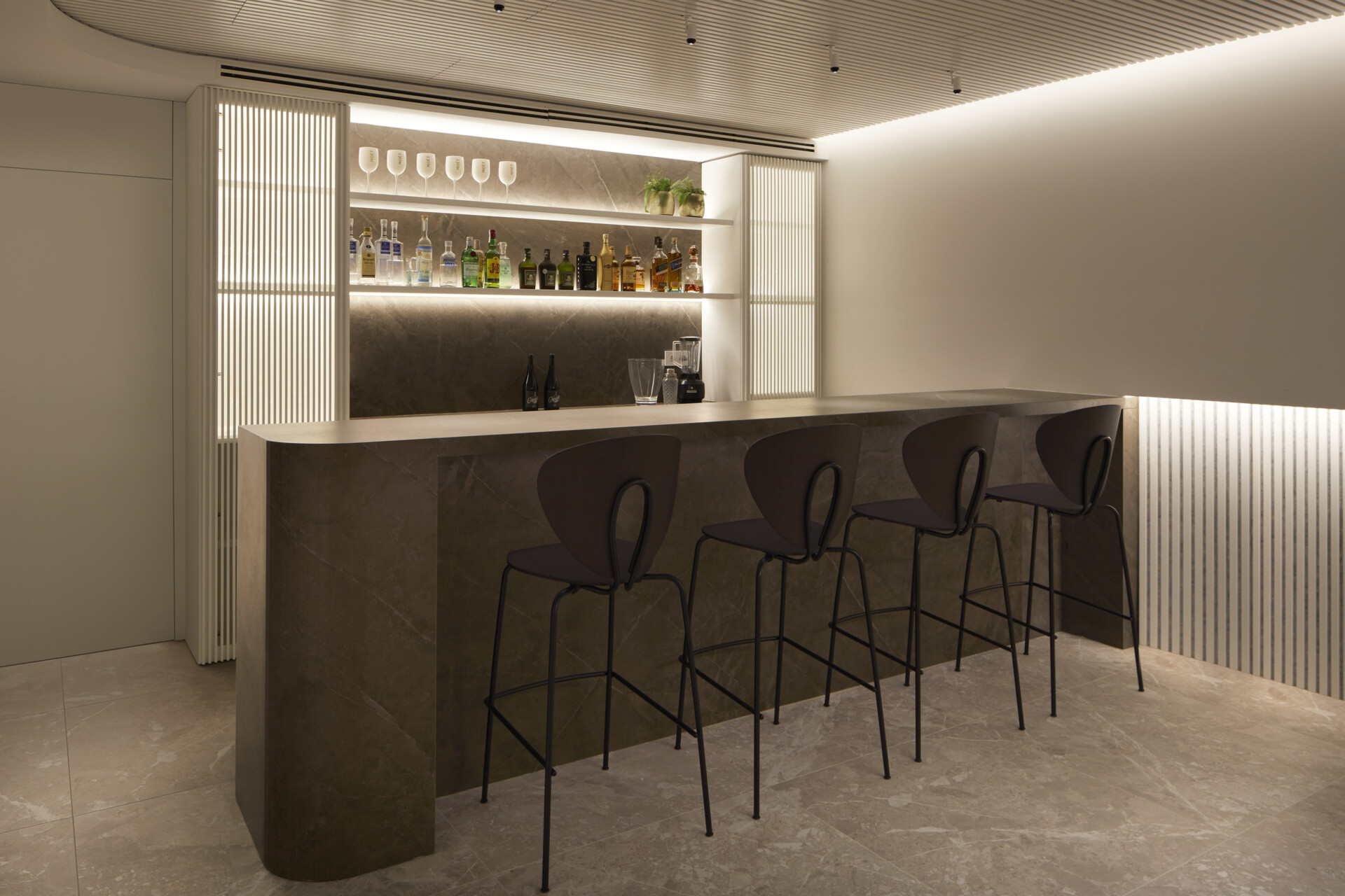 A multipurpose room made for ease, with home bar with hidden highlight, a tufted sofa, foosball table, and soft artwork lending the space a laid-back, lounge-like rhythm. Ribbed details and stone tiles carry the material palette through with texture and warmth.