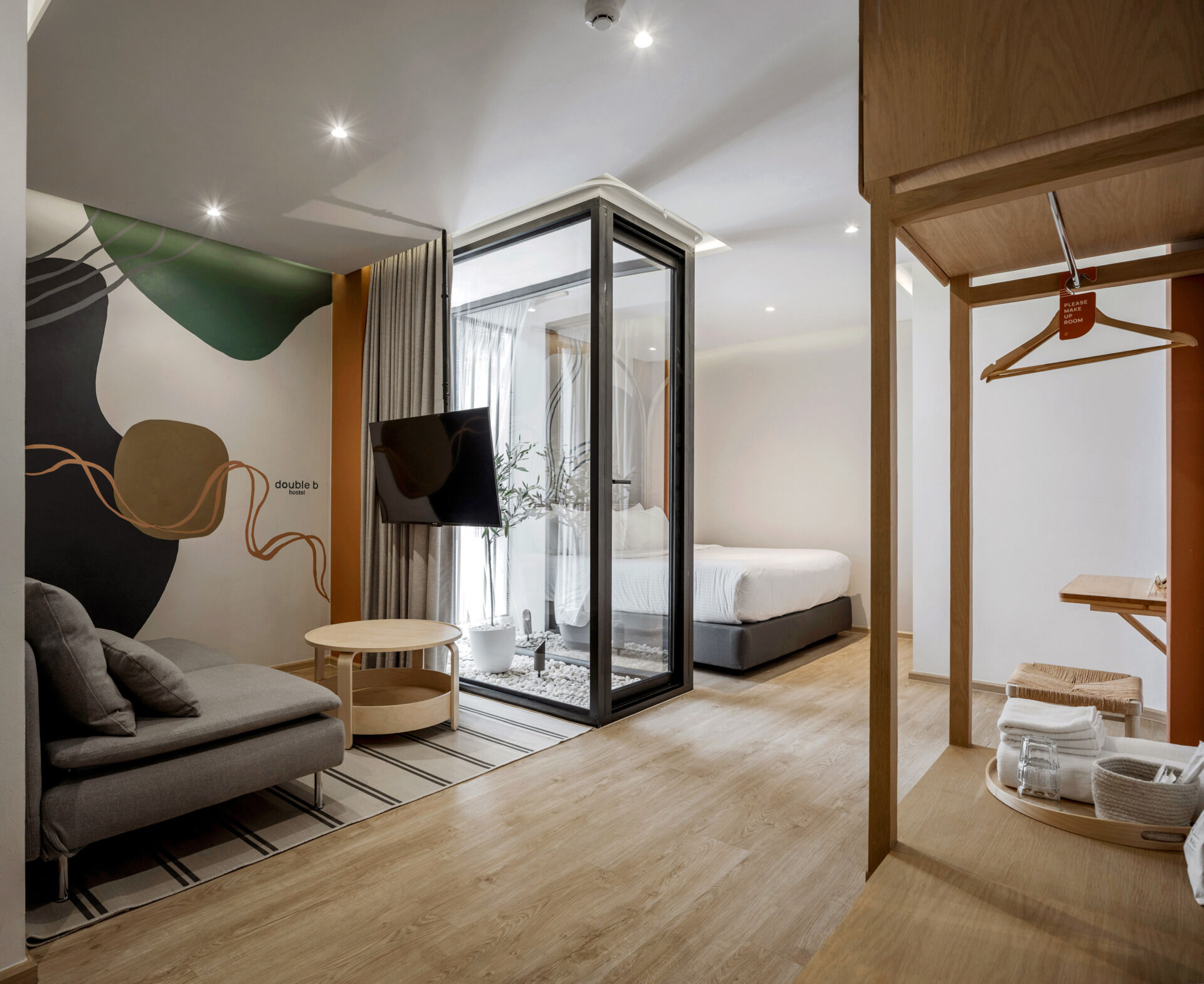 In this modern hostel, guest rooms range from private suites to shared dorm-style spaces with bunk beds, each designed with the same attention to warmth and simplicity found throughout the hostel. Wood accents carry through in the form of open wardrobes, built-in desks, and shelving, maintaining a consistent material language from the common areas. Whether private or shared, each room feels grounded and intentional, offering a calm retreat from the surrounding city.