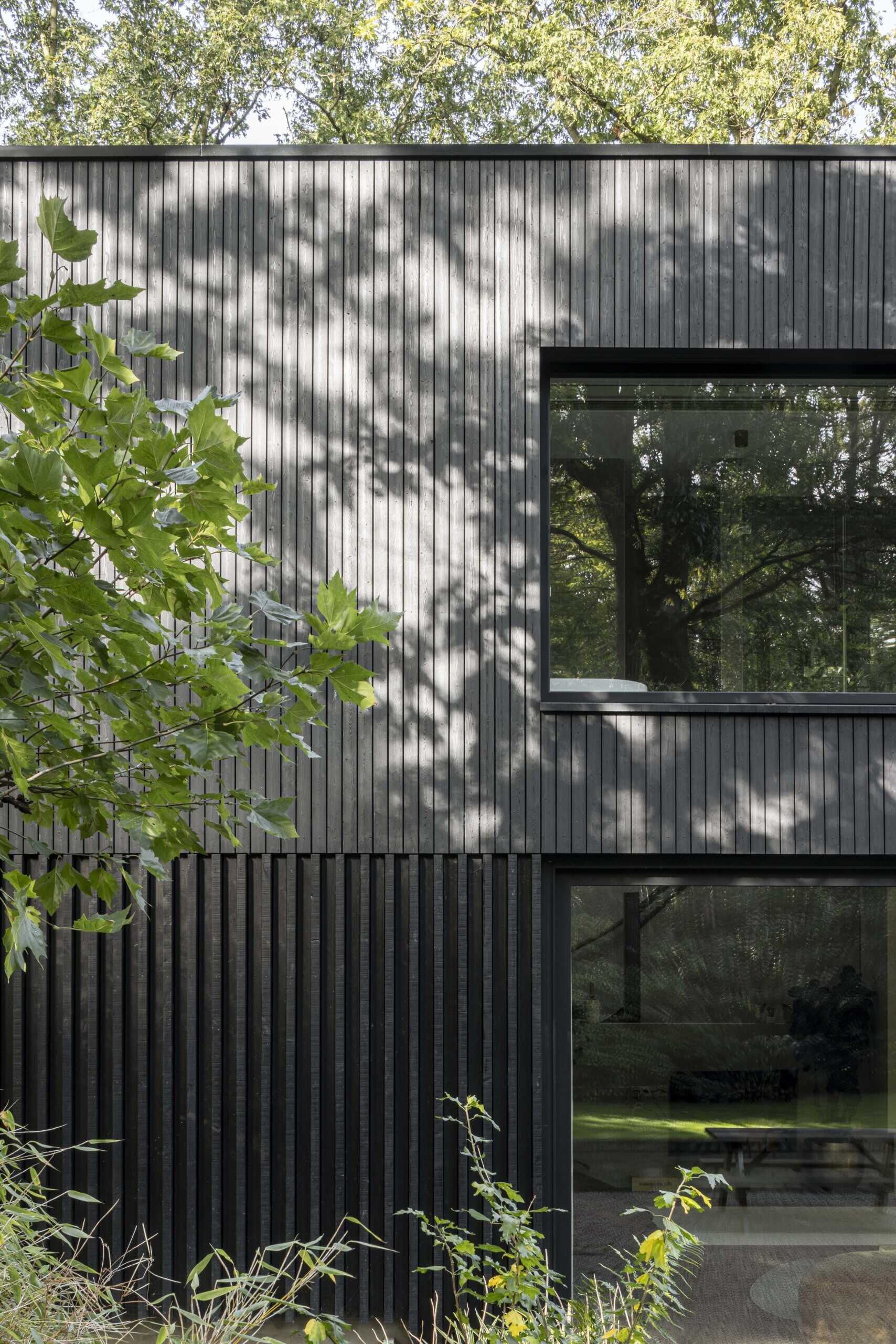 This striking modern home showcases the power of simplicity through its dark wood cladding and clean, rectangular form. Vertical wood slats add texture and rhythm to the facade, while the deep black finish helps the structure blend seamlessly into its natural surroundings. Generously sized windows are thoughtfully positioned to capture views of the landscape and invite daylight into the interior, all while maintaining the home’s strong architectural lines. 