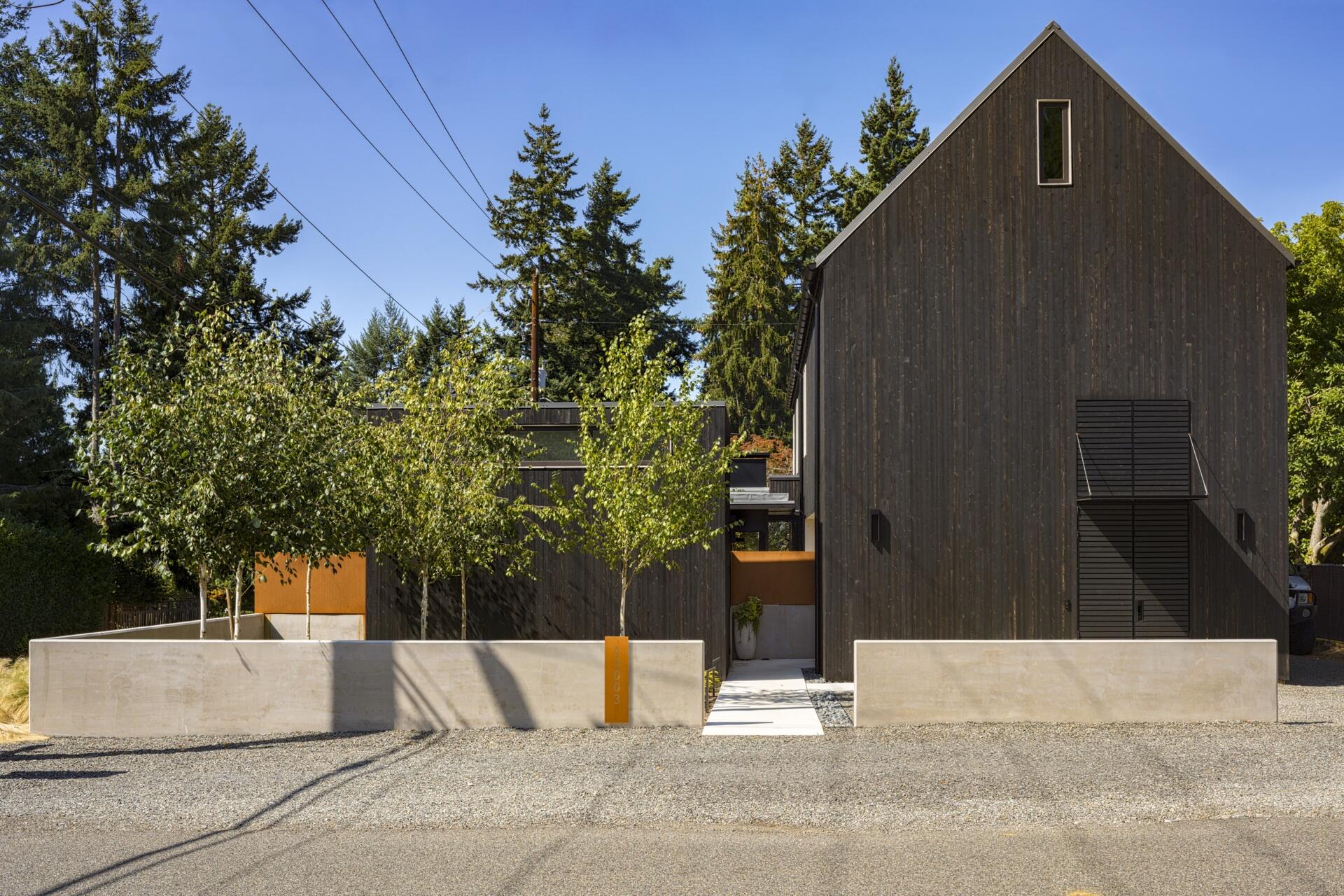 Exterior wood siding of this modern house is treated with black pine tar, creating a durable, textured finish that visually anchors the building. Corten steel accents add warmth and material contrast without disrupting the minimalist language.