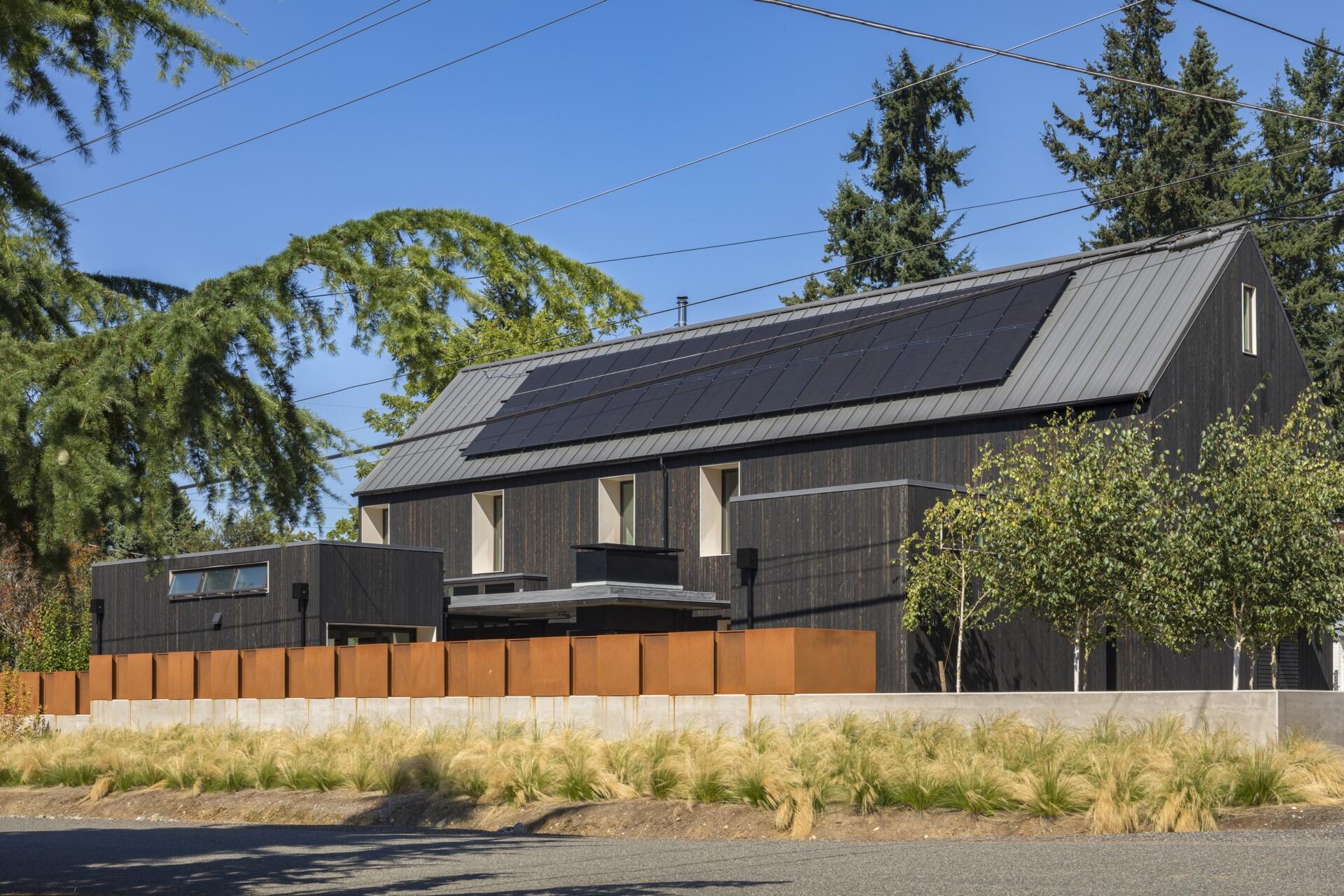 Exterior wood siding of this modern house is treated with black pine tar, creating a durable, textured finish that visually anchors the building. Corten steel accents add warmth and material contrast without disrupting the minimalist language.