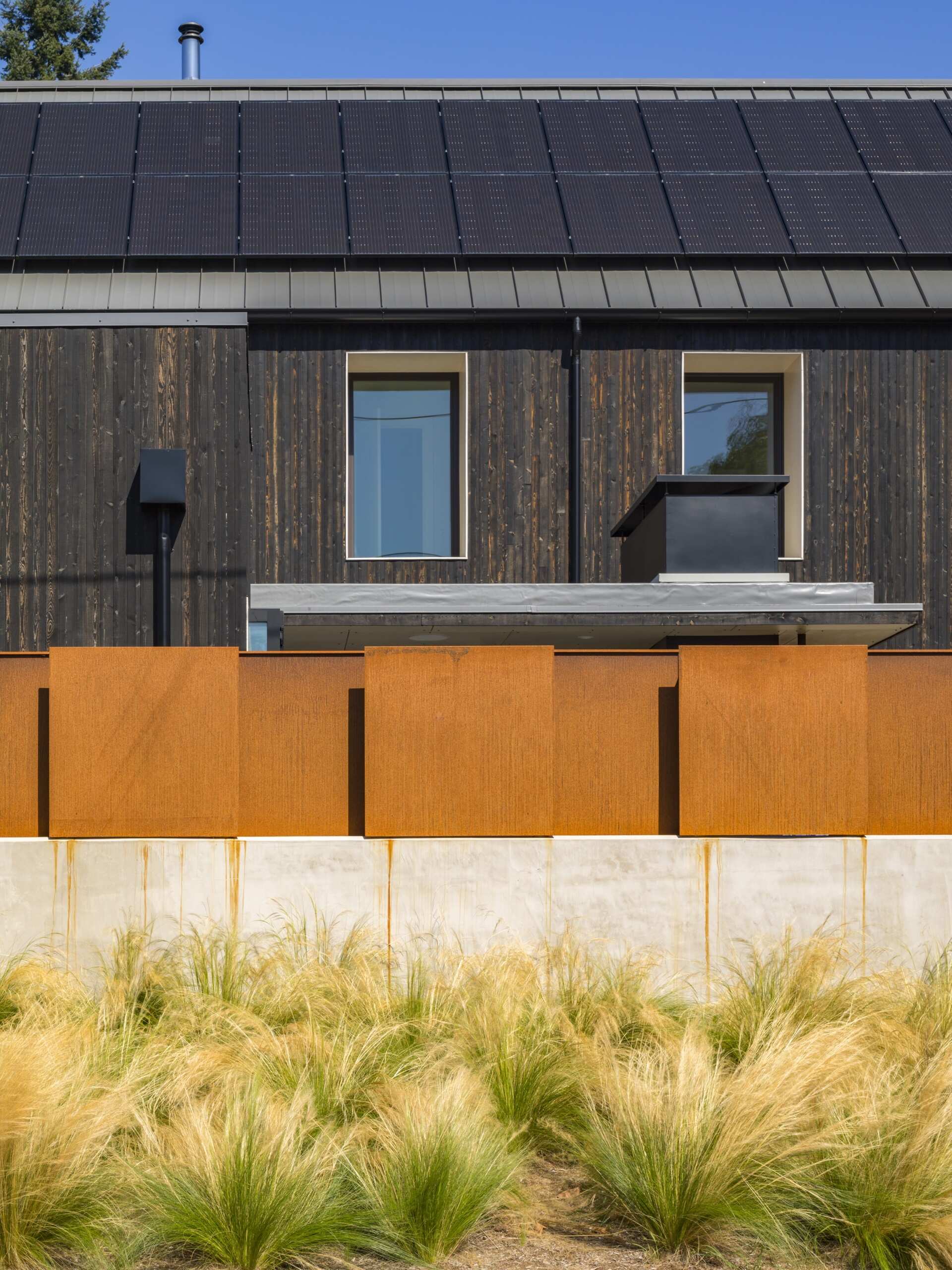 Exterior wood siding of this modern house is treated with black pine tar, creating a durable, textured finish that visually anchors the building. Corten steel accents add warmth and material contrast without disrupting the minimalist language.