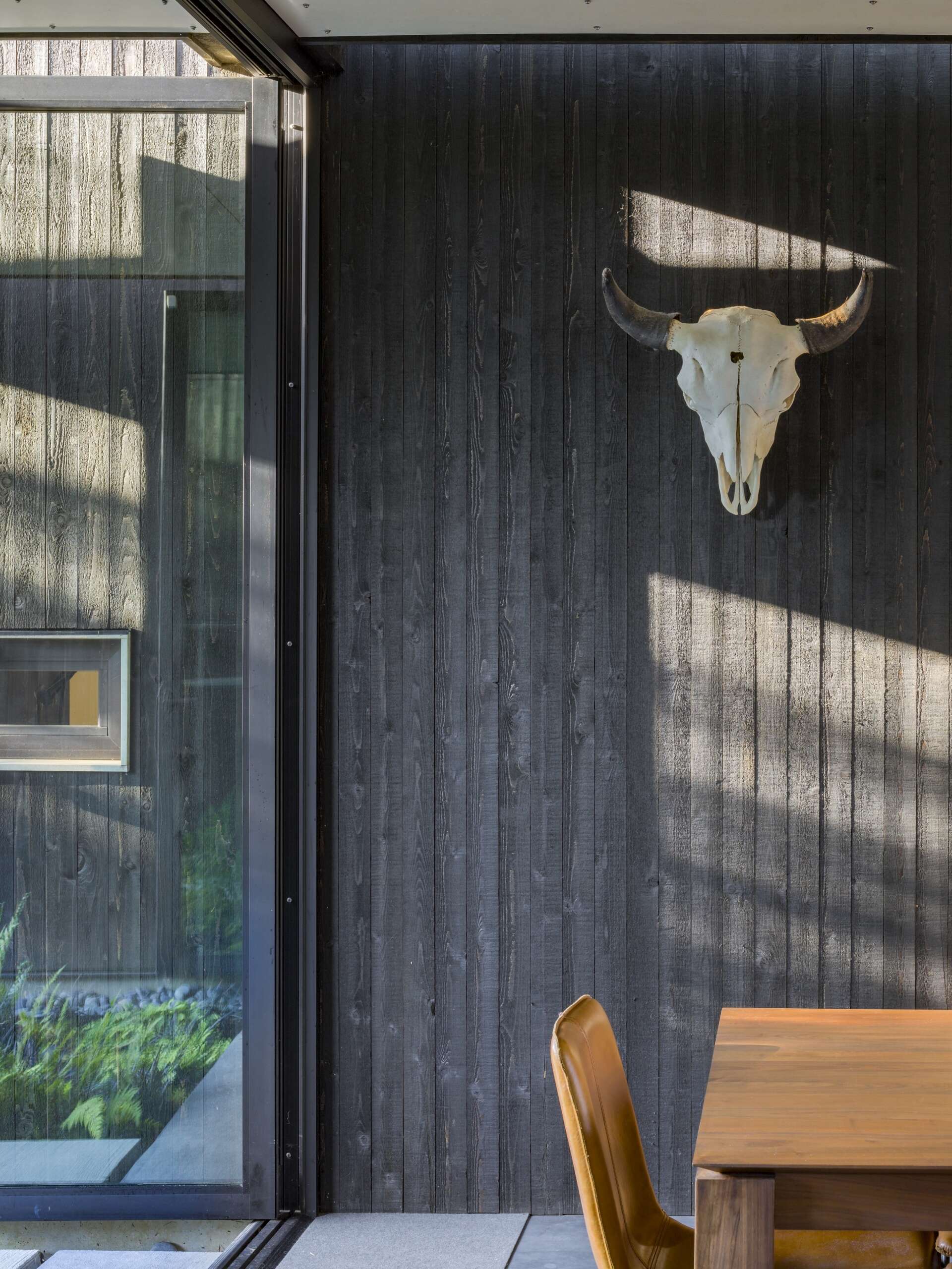 This modern dining room features oversized glass doors that open fully to the courtyard. These doors erase boundaries between inside and out while drawing in diffuse light. The roof appears to float above the space, supported by hidden connections and integrated lighting.