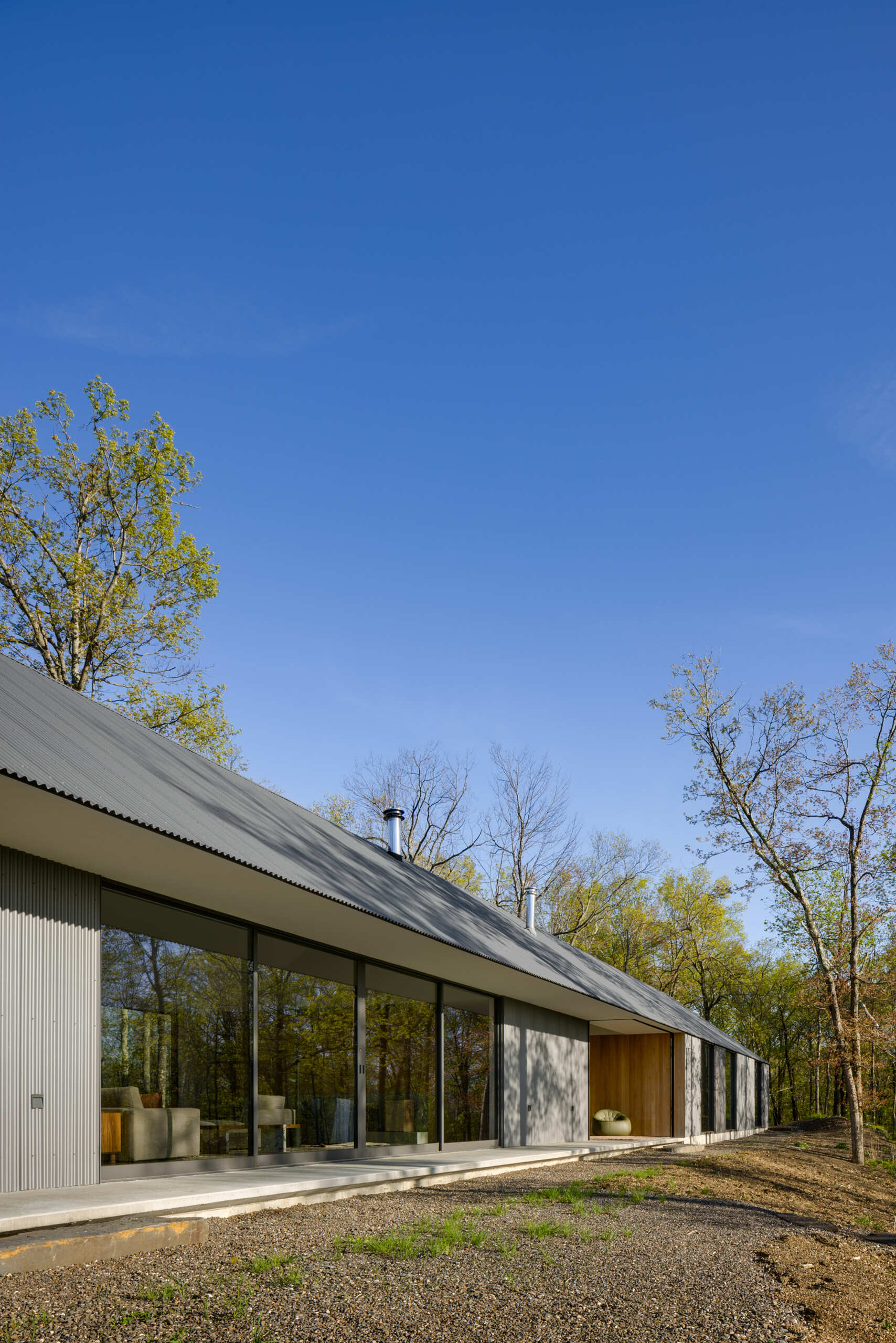 Ridge House blends clean gabled architecture with corrugated metal and board-formed concrete, creating a striking yet natural presence that weathers gracefully within its wooded ridgeline setting.