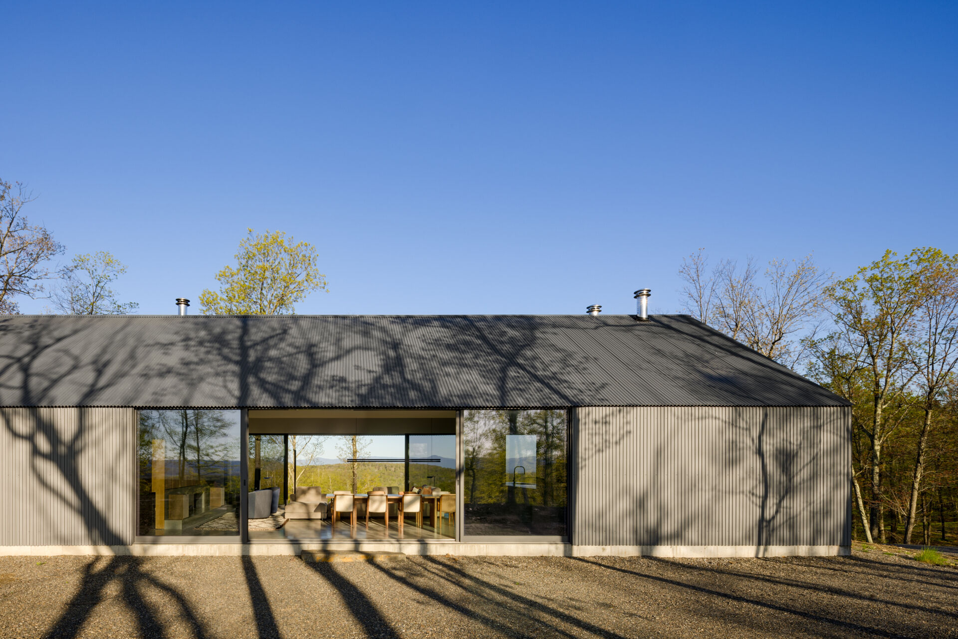 Ridge House blends clean gabled architecture with corrugated metal and board-formed concrete, creating a striking yet natural presence that weathers gracefully within its wooded ridgeline setting.