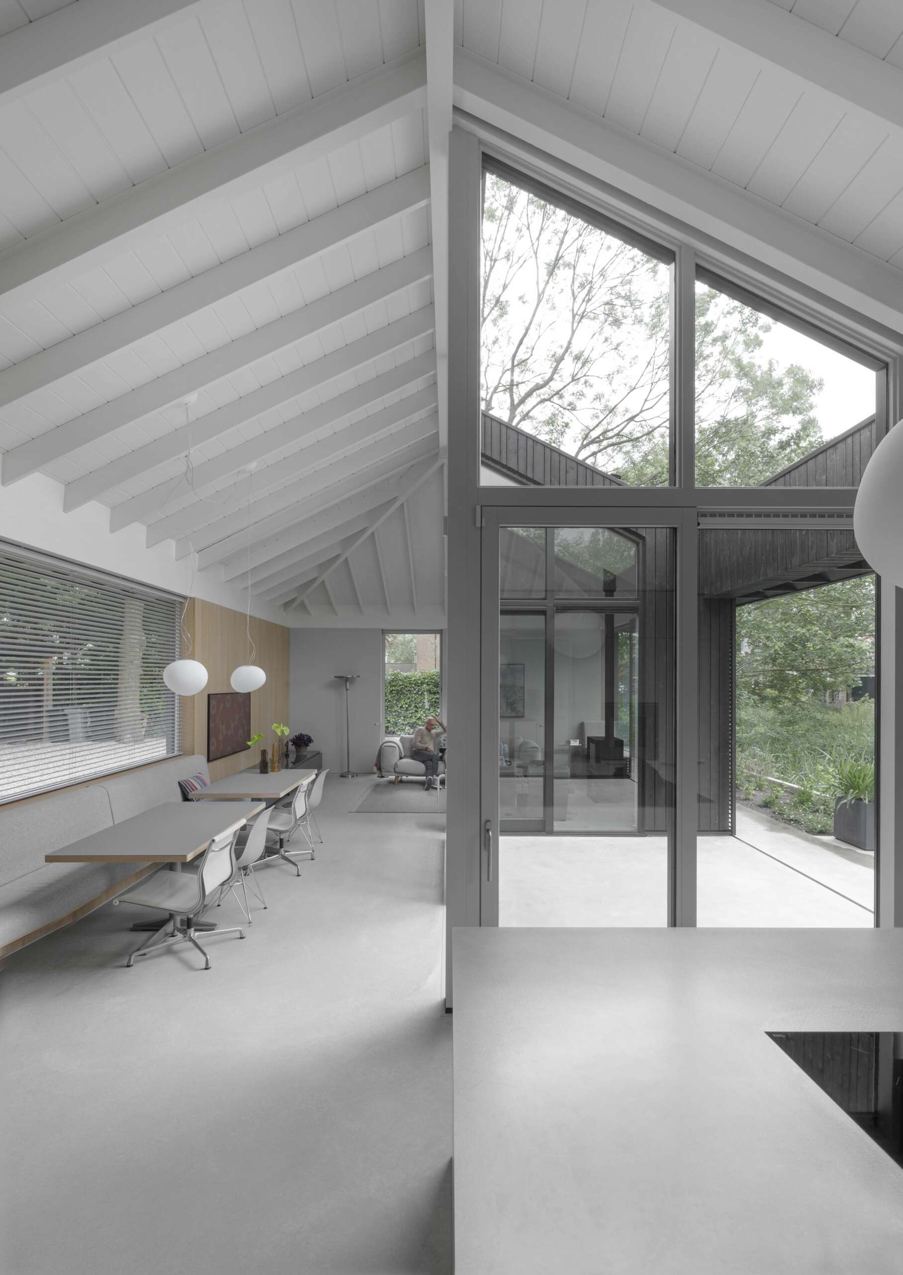 Positioned between the kitchen and living room, this dining area feels airy and yet intimate. A built-in banquette stretches along the wall, while tables and sleek white chairs keep the space light and open, with two minimal pendant lights suspended above for gentle illumination.
