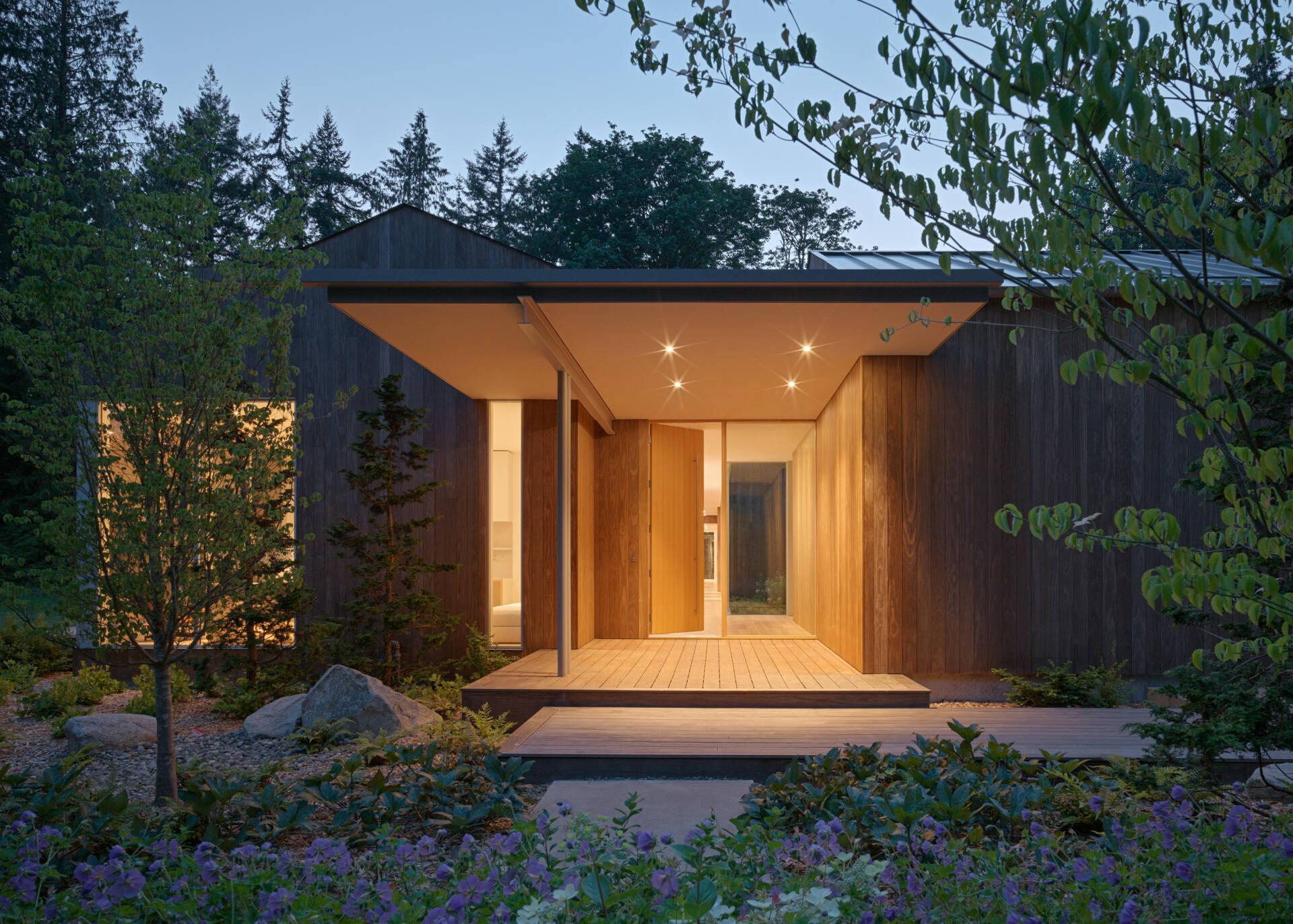 The approach to this modern home winds through preserved native trees, leading to an entry sequence made of poured-in-place concrete pavers and matching wood decking. These materials create continuity between landscape and architecture.