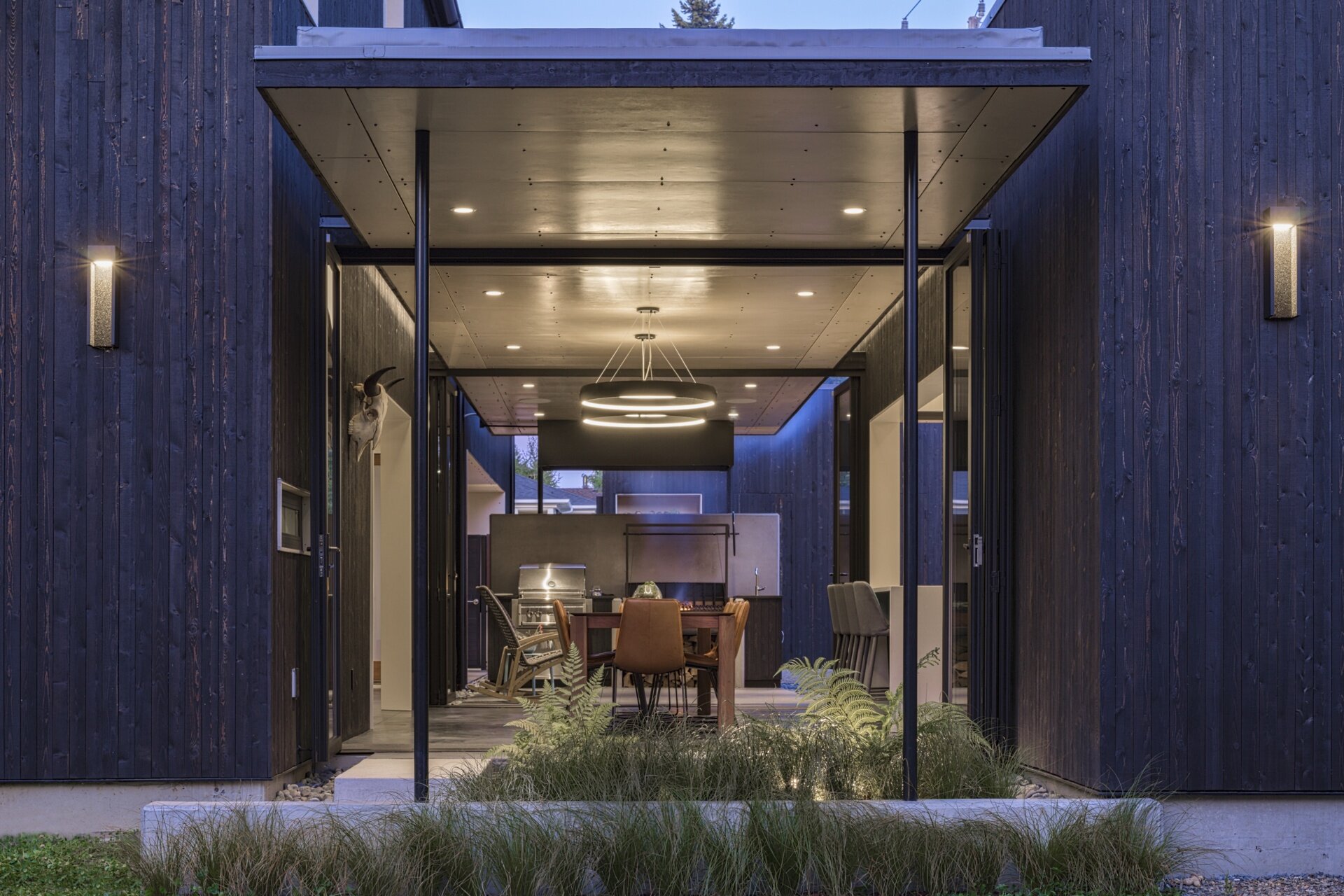 This modern dining room features oversized glass doors that open fully to the courtyard. These doors erase boundaries between inside and out while drawing in diffuse light. The roof appears to float above the space, supported by hidden connections and integrated lighting.