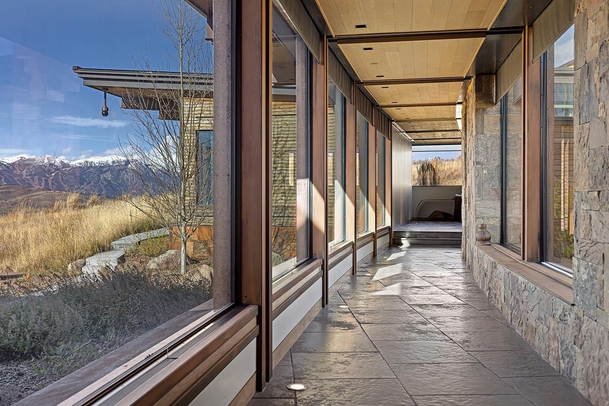 Sunlight spills into this glass-lined hallway, casting soft reflections on the textured stone floor and warming the neutral tones of wood and stone. With views stretching out to golden grasses and distant peaks, the space feels more like a quiet nature walk than a passage between rooms. Gentle shadows shift throughout the day, creating a rhythm that mirrors the landscape outside. It’s a peaceful, almost meditative place—perfect for pausing, breathing deep, and watching the light change.