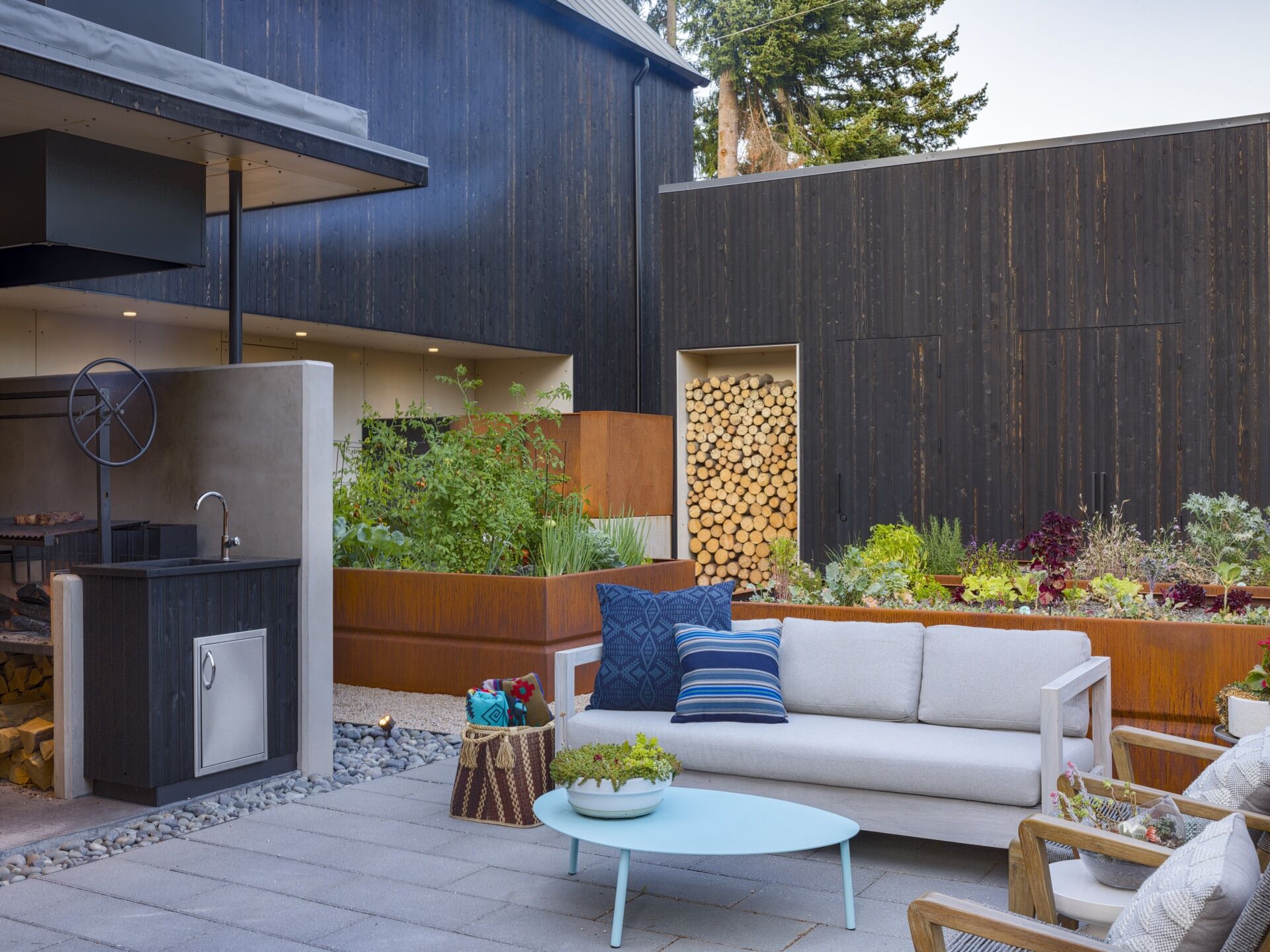 Positioned between the three volumes, the courtyard acts as an outdoor living room and features a kitchen, firewood storage, and large corten steel planters.