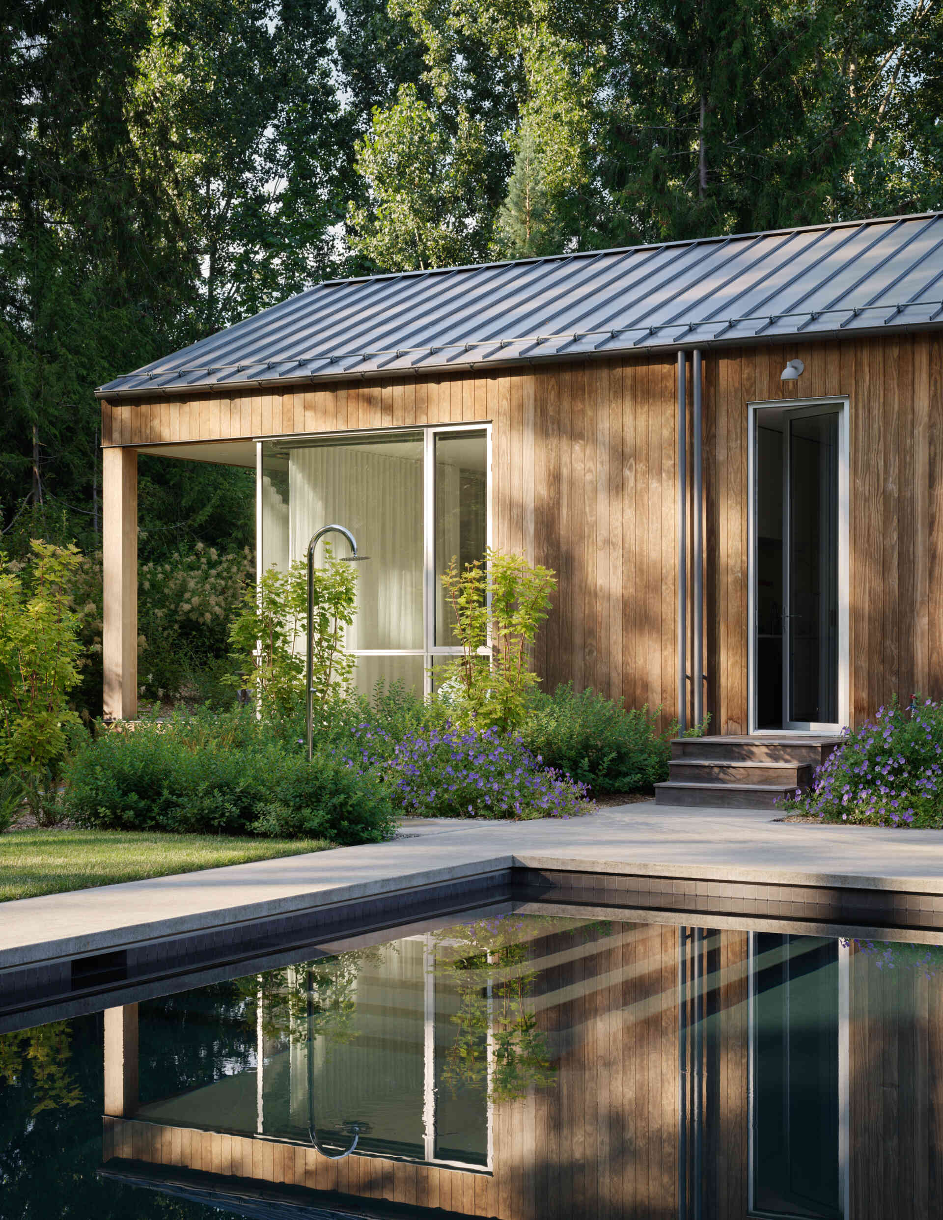 Outdoor life at this modern home is central to the family's daily rhythm. A generous lawn stretches out from the home, giving space for play and relaxation. At its far edge, a swimming pool and spa sit in full sun, paired with a stone-paved lounging terrace and outdoor shower.