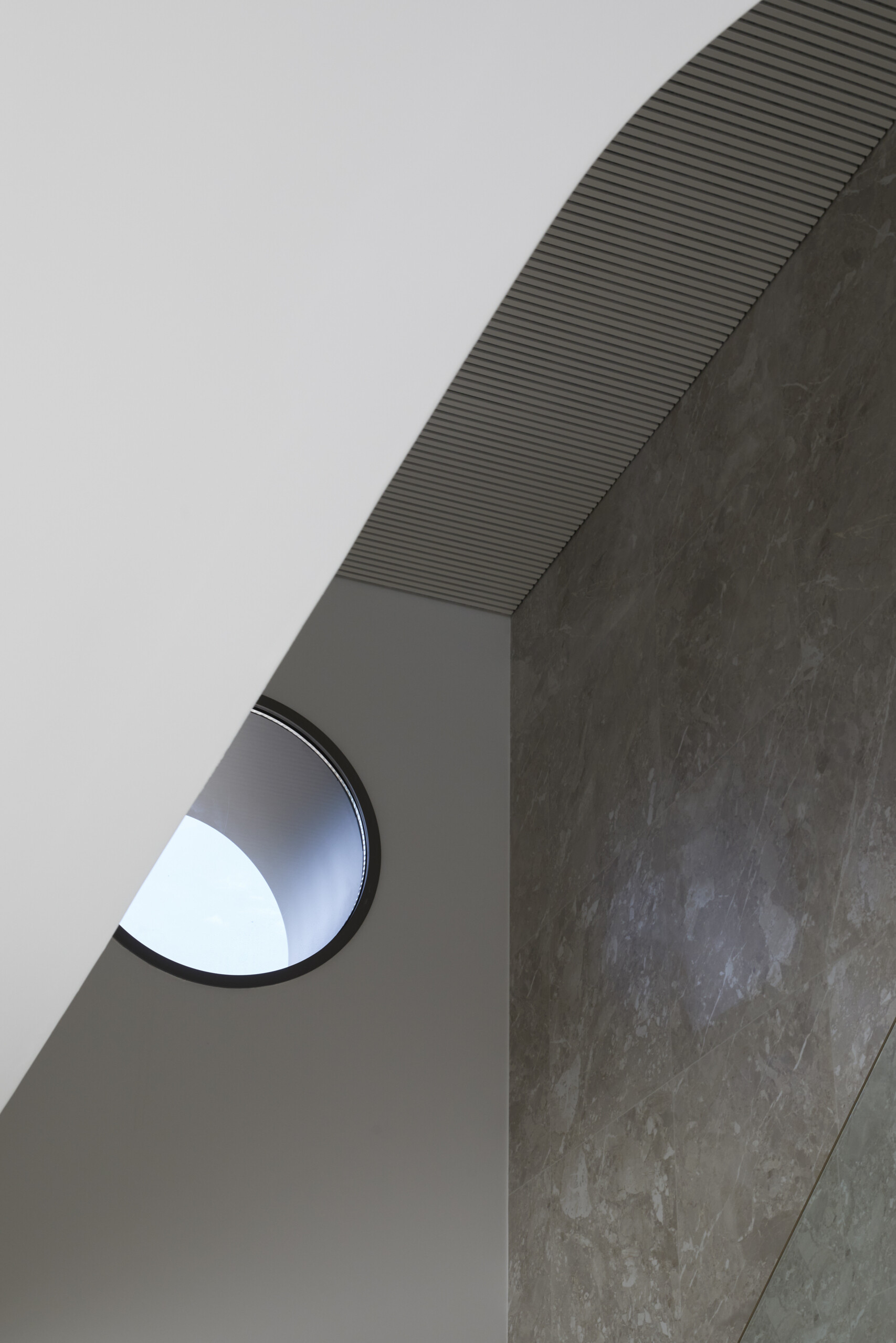 The entryway pairs architectural drama with quiet restraint. A tall charcoal door sits beneath a sculptural ceiling and round skylight, while built-in shelves and natural finishes offer a warm, curated welcome.