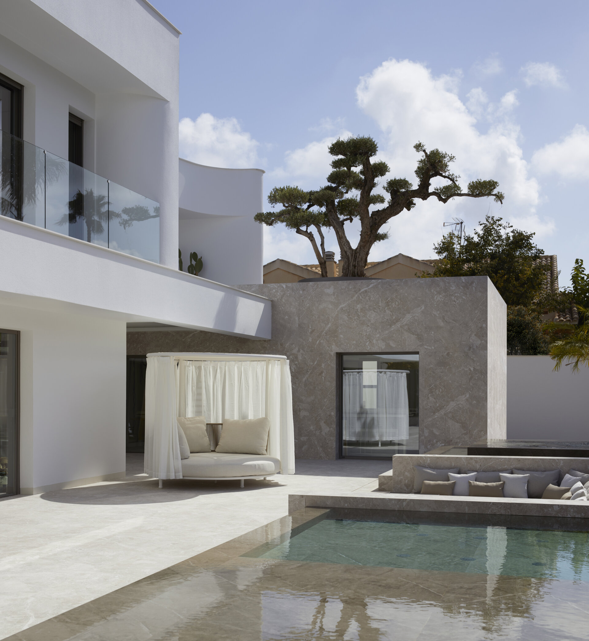 A round daybed tucked beneath airy white drapes offers a private, shaded spot perfect for quiet afternoons or leisurely reading, while a recessed lounge with neutral-toned cushions nestles into the landscape, creating a cozy nook for conversation beside the pool.