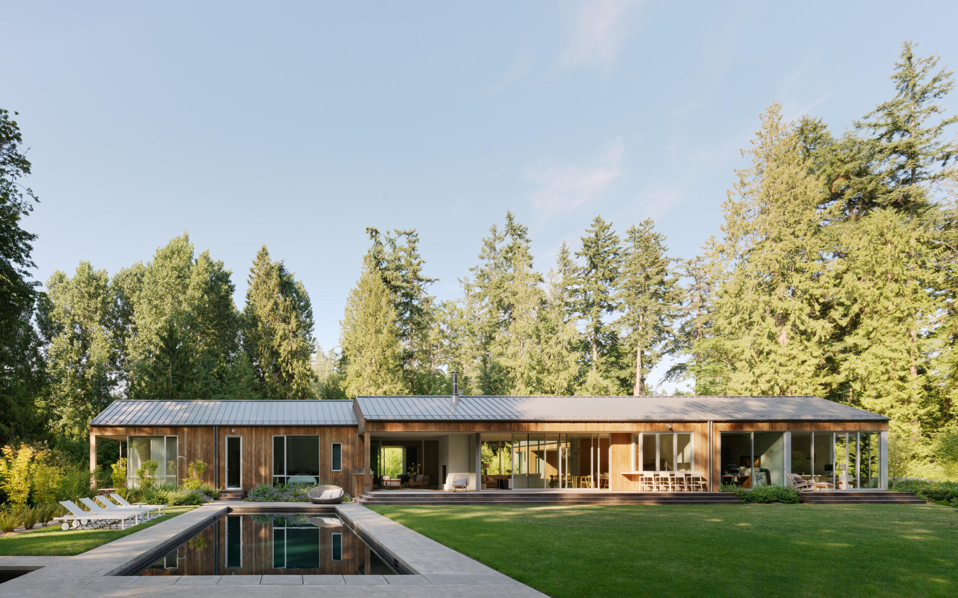 The house presents a trio of connected, gabled volumes clad in vertical Kebony siding, a thermally modified wood that weathers over time into a soft gray. The gabled metal roofs drain into exposed half-round gutters, combining clean lines with durable function. 
