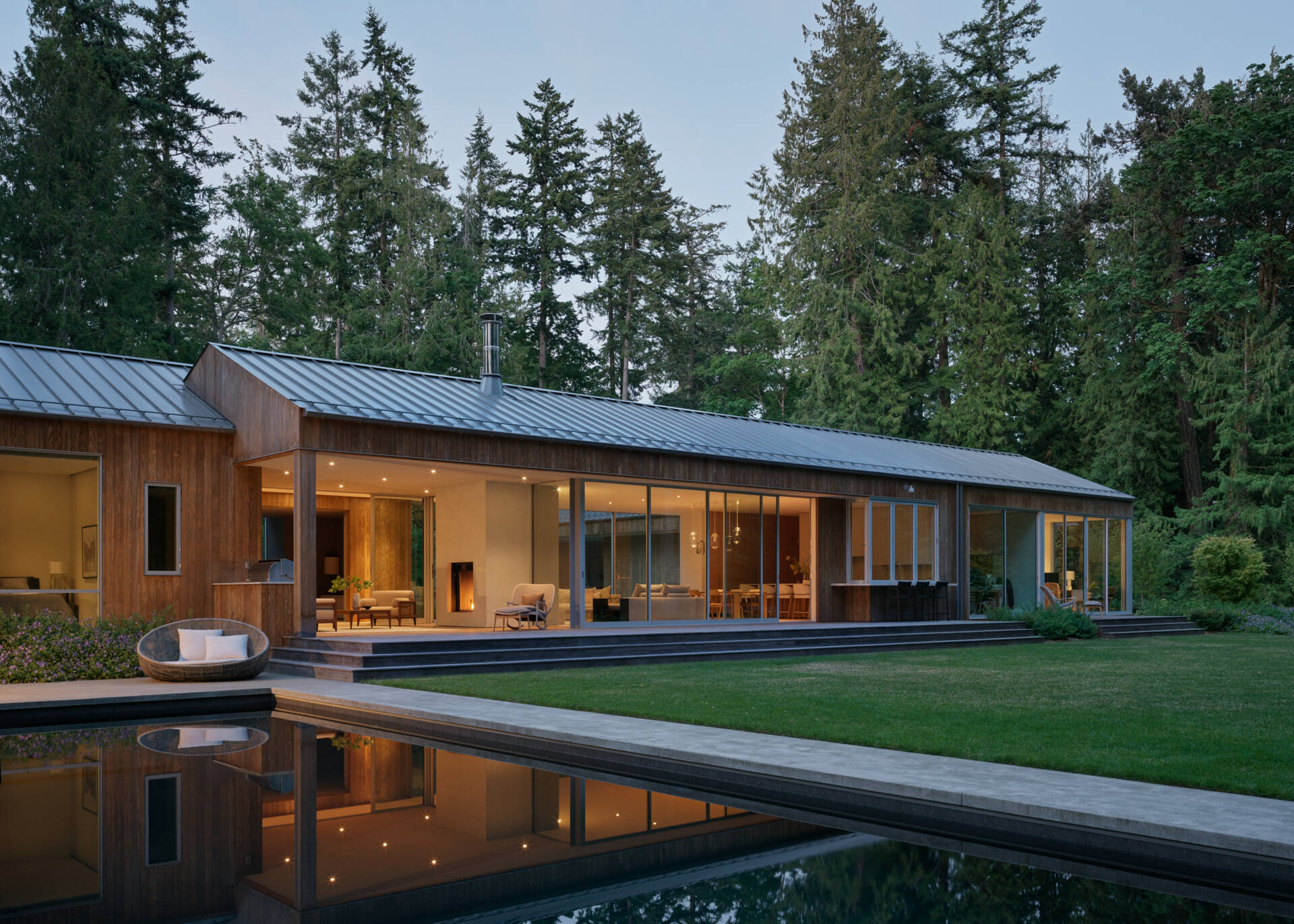 The house presents a trio of connected, gabled volumes clad in vertical Kebony siding, a thermally modified wood that weathers over time into a soft gray. The gabled metal roofs drain into exposed half-round gutters, combining clean lines with durable function. 