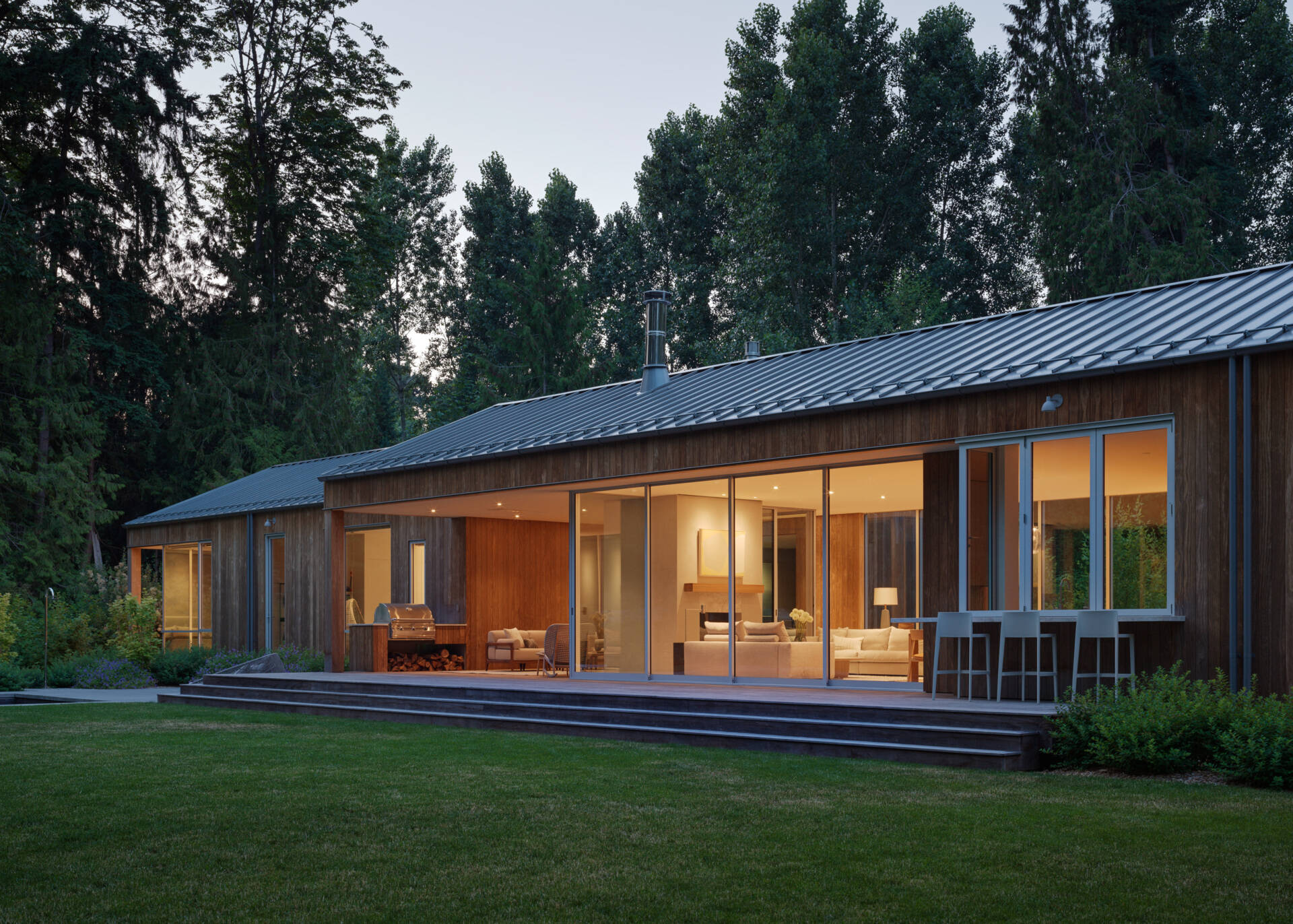 The house presents a trio of connected, gabled volumes clad in vertical Kebony siding, a thermally modified wood that weathers over time into a soft gray. The gabled metal roofs drain into exposed half-round gutters, combining clean lines with durable function. 