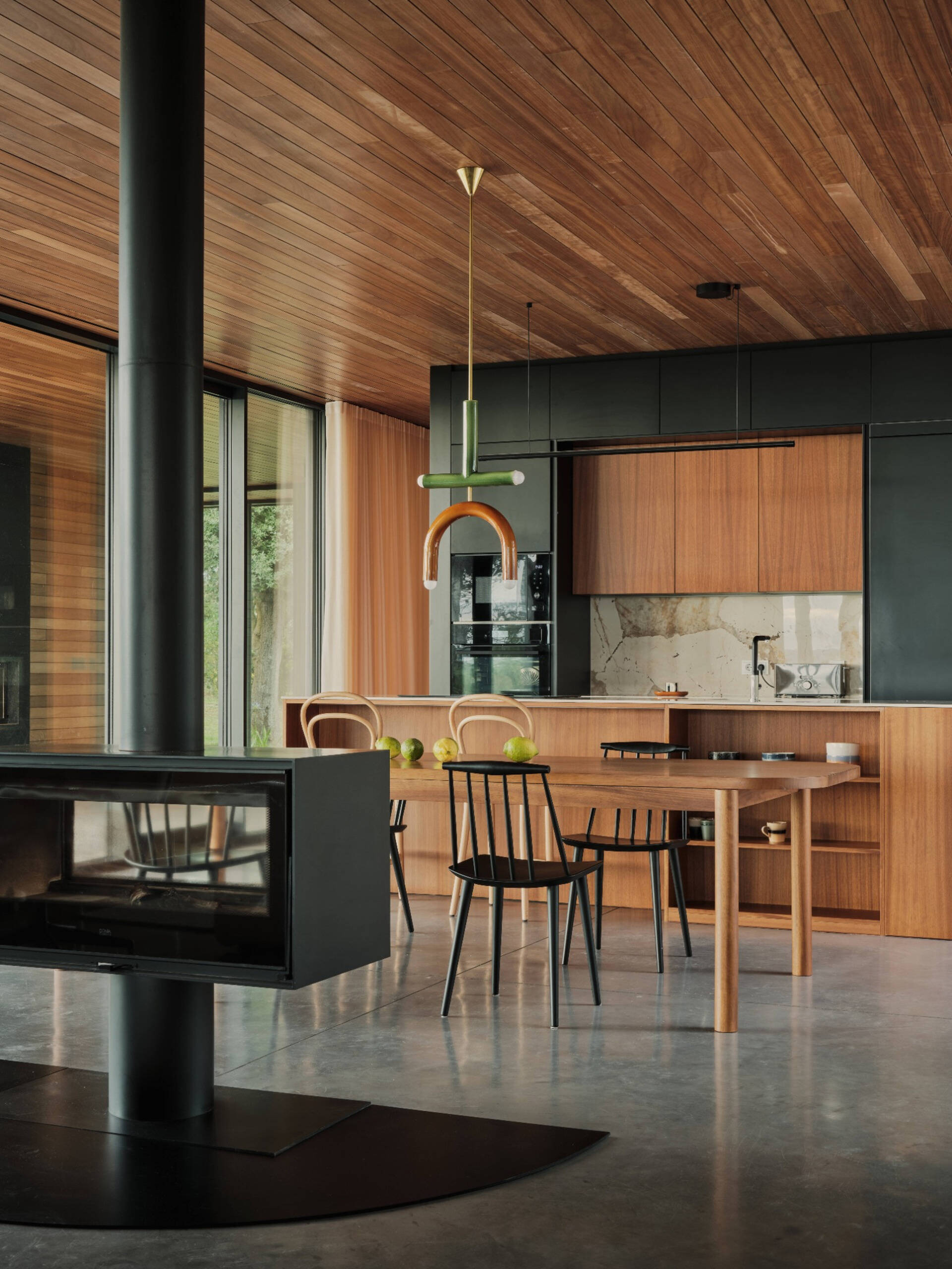 This kitchen features a striking wall of dark cabinets, contrasted by a wood island with open shelving. High-quality materials with natural textures complement the home’s overall palette, creating a warm yet refined atmosphere.
