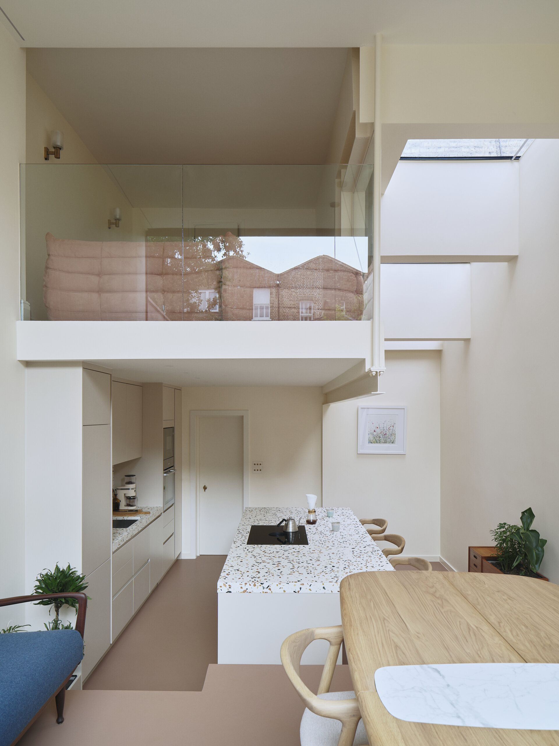 Above the kitchen, a glazed mezzanine loft offers a quiet, elevated retreat while maintaining visual connection to the rest of the home. Positioned to overlook the double-height living area, it allows light to pass through freely, enhancing the sense of openness. This suspended space can function as a reading nook, workspace, or lounge