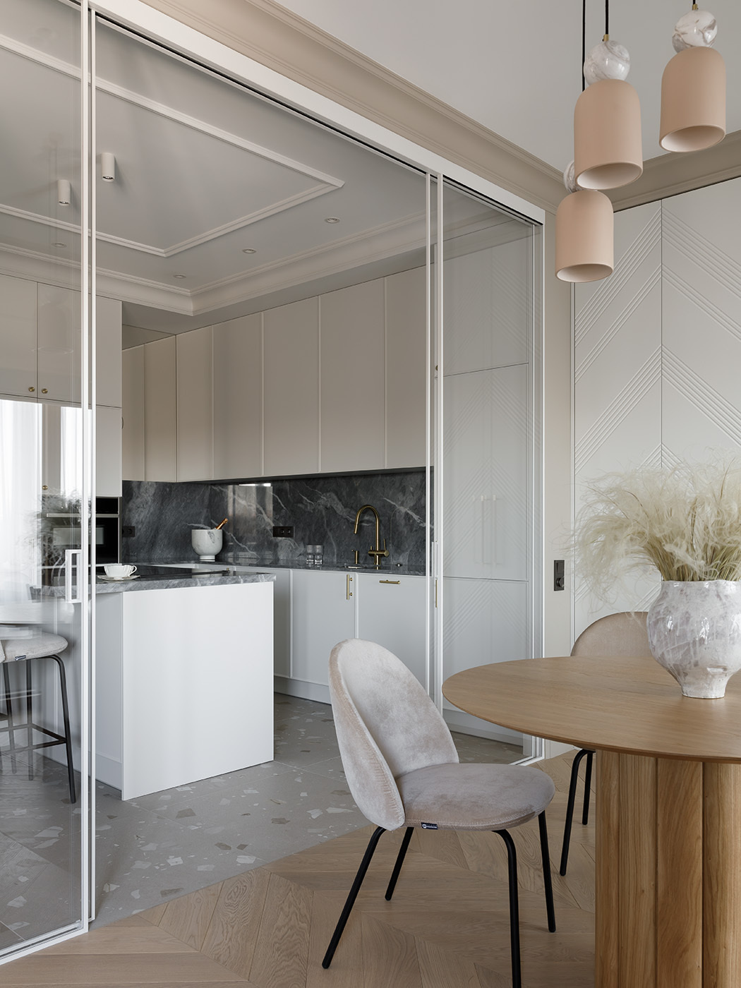 A sculptural, custom-designed kitchen blends function and elegance with seamless cabinetry, natural marble, and sleek Asko appliances. A mirror subtly enhances the light, while a matching island with minimalist stools creates a casual gathering spot. A sliding glass partition offers flexible separation from the dining area.