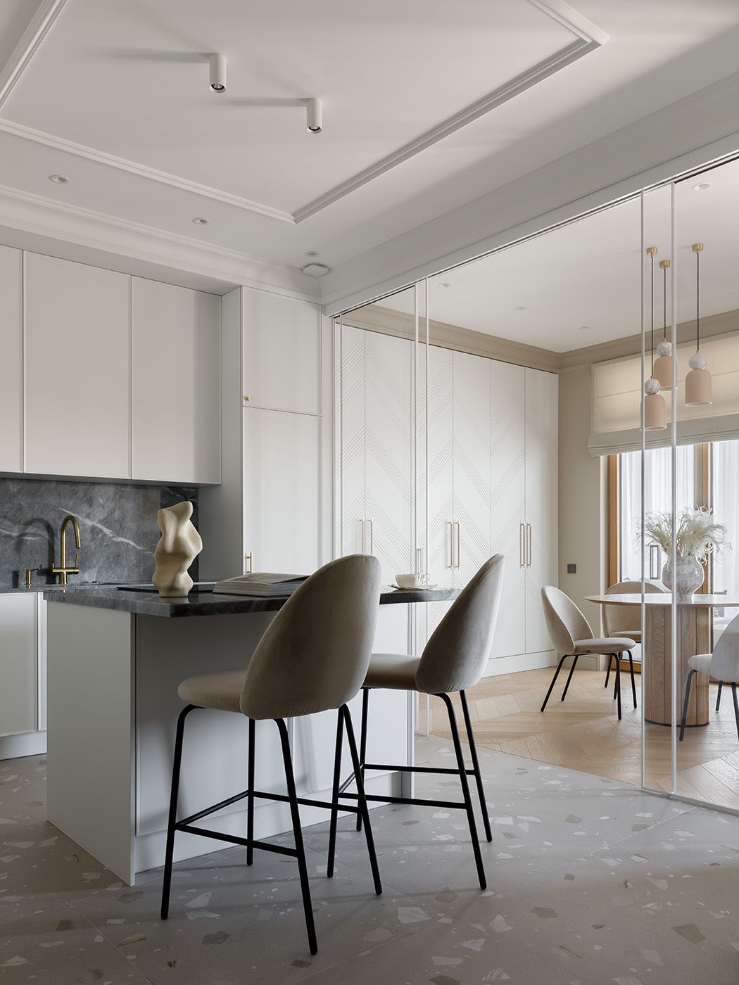 A sculptural, custom-designed kitchen blends function and elegance with seamless cabinetry, natural marble, and sleek Asko appliances. A mirror subtly enhances the light, while a matching island with minimalist stools creates a casual gathering spot. A sliding glass partition offers flexible separation from the dining area.