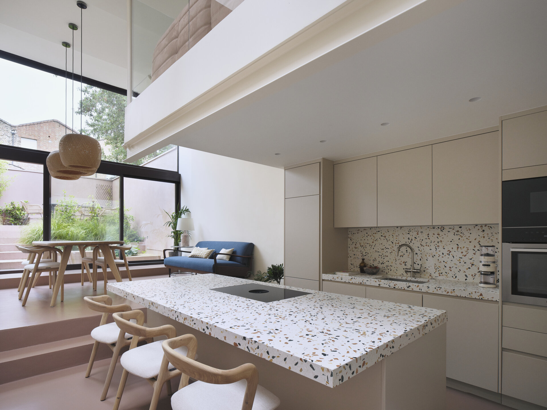 The kitchen features a clean, integrated design with hardware-free cabinetry that complements the home’s minimalist material palette. Terrazzo countertops introduce color and variation, adding a subtle sense of play. A central island anchors the room, providing ample space for cooking and casual dining while preserving open views toward the dining area and terrace.