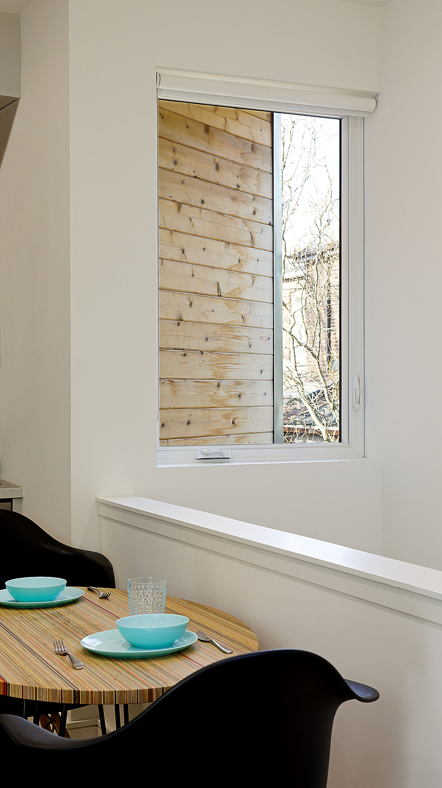 The dining area of this modern laneway house features a round wooden table with two chairs, framed by soft light that spills in from multiple angles.
