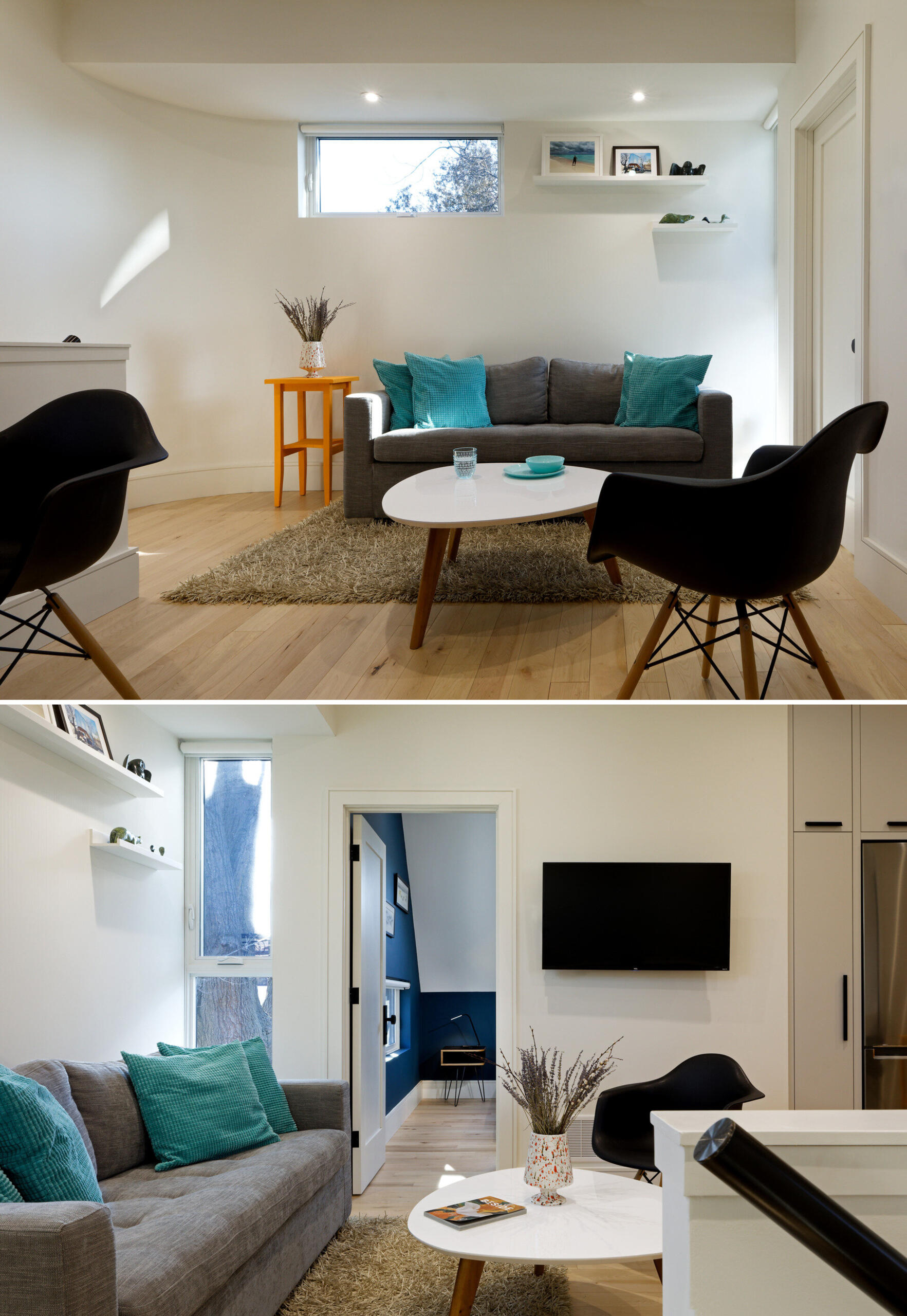 Wood floors run throughout this laneway home, grounding each space with natural warmth. In the living area, a small grey couch is dressed with turquoise accent pillows. Above it, a narrow horizontal window lets in gentle daylight, while a pair of floating white shelves display personal objects and art. A tall vertical window beside the bedroom door adds a bright moment to the transition between spaces.
