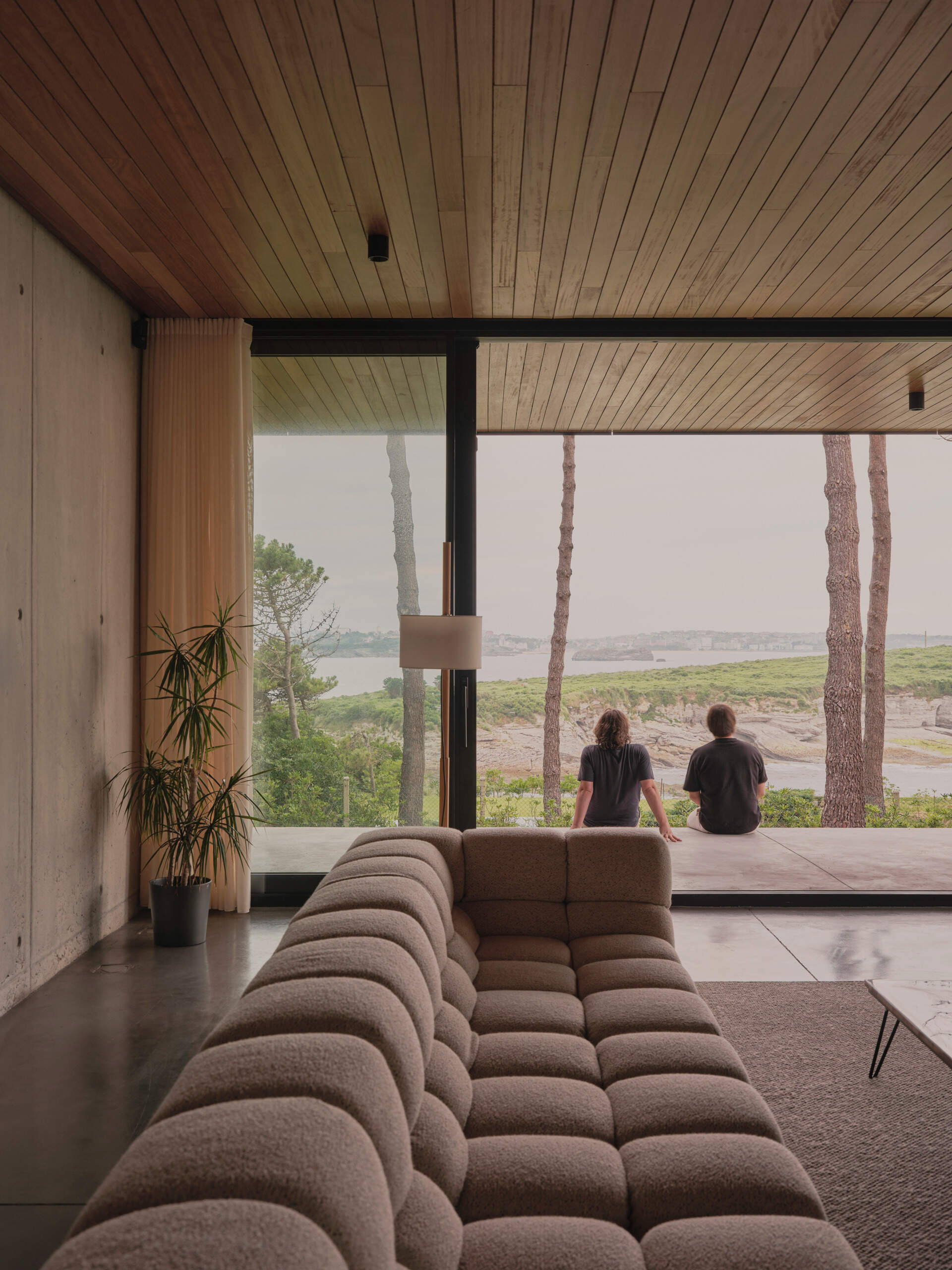 Slatted wood ceilings continue indoors, creating visual continuity with the landscape and echoing the home’s directional emphasis. The seamless integration of living, dining, and kitchen spaces reflects a contemporary approach to open-plan living, while materials and details root the experience firmly in place.