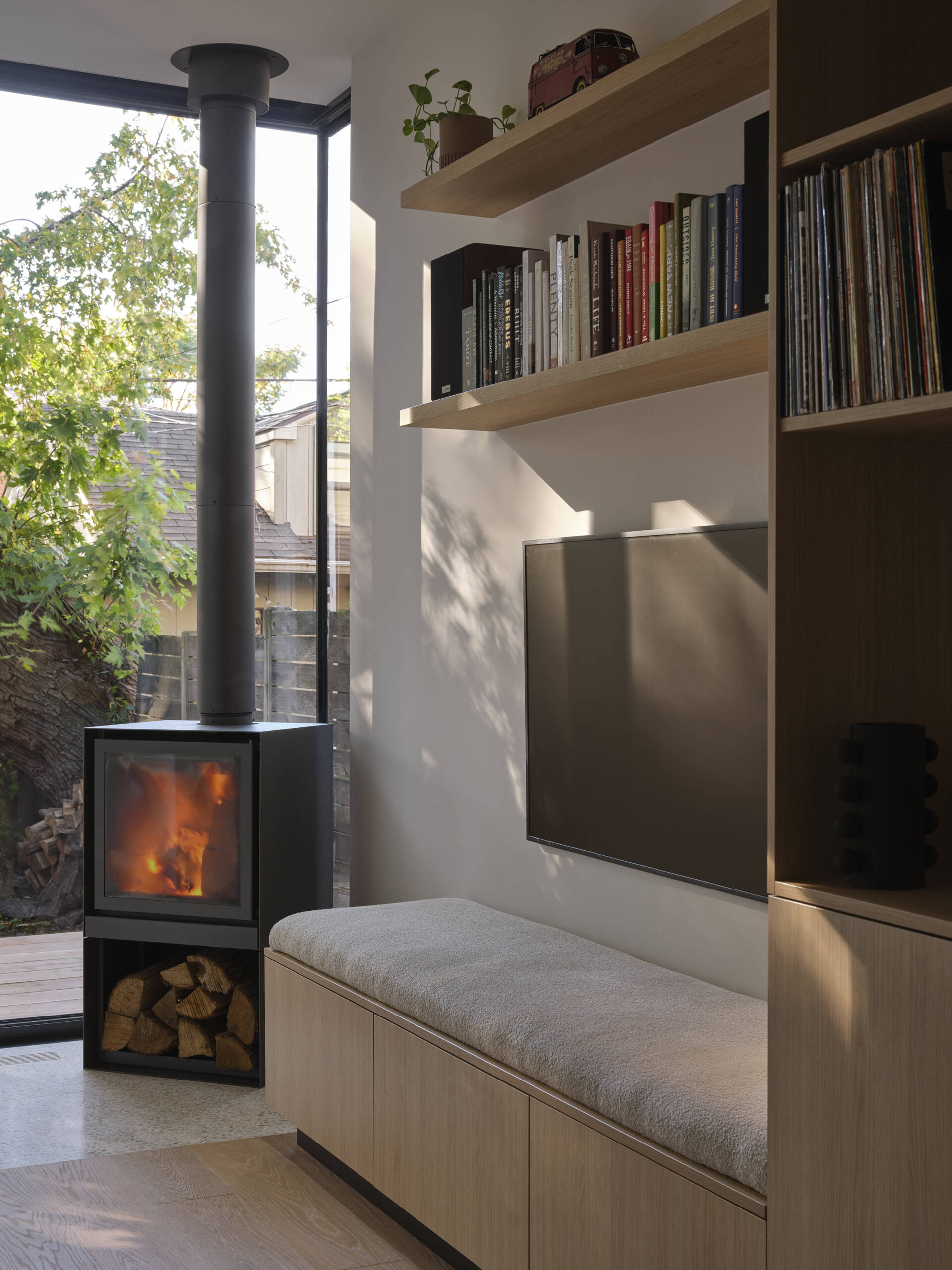 A custom oak media unit with built-in seating adds warmth and functionality to this open plan living space with a wood-burning fireplace.