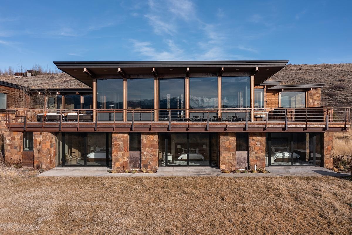 Nestled into the hillside like it naturally belongs there, this home embraces its mountain surroundings with a rugged elegance. The living roof, blanketed in grass, blends almost seamlessly into the wild landscape, while stacked stone walls ground the structure with earthy warmth. Generous windows invite the panoramic views inside, offering a daily dose of the snow-capped peaks beyond. It's the kind of place that feels both tucked away and wide open, perfect for quiet mornings or evenings that stretch out under the stars.