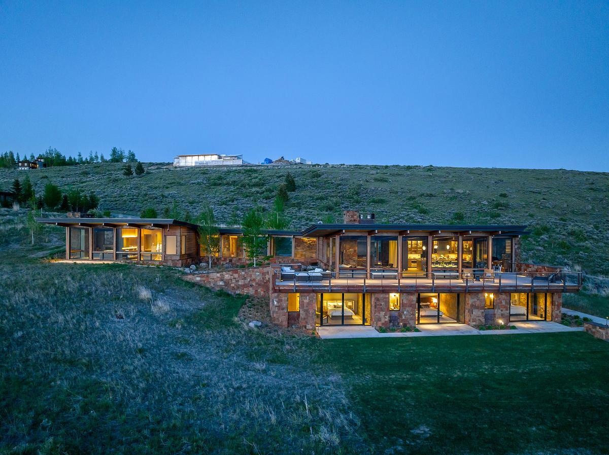 At night, the house glows softly against the hillside, its warm interior light spilling through expansive windows and casting a gentle glow onto the surrounding landscape. From a distance, it feels almost like a quiet lantern tucked into the slope.
