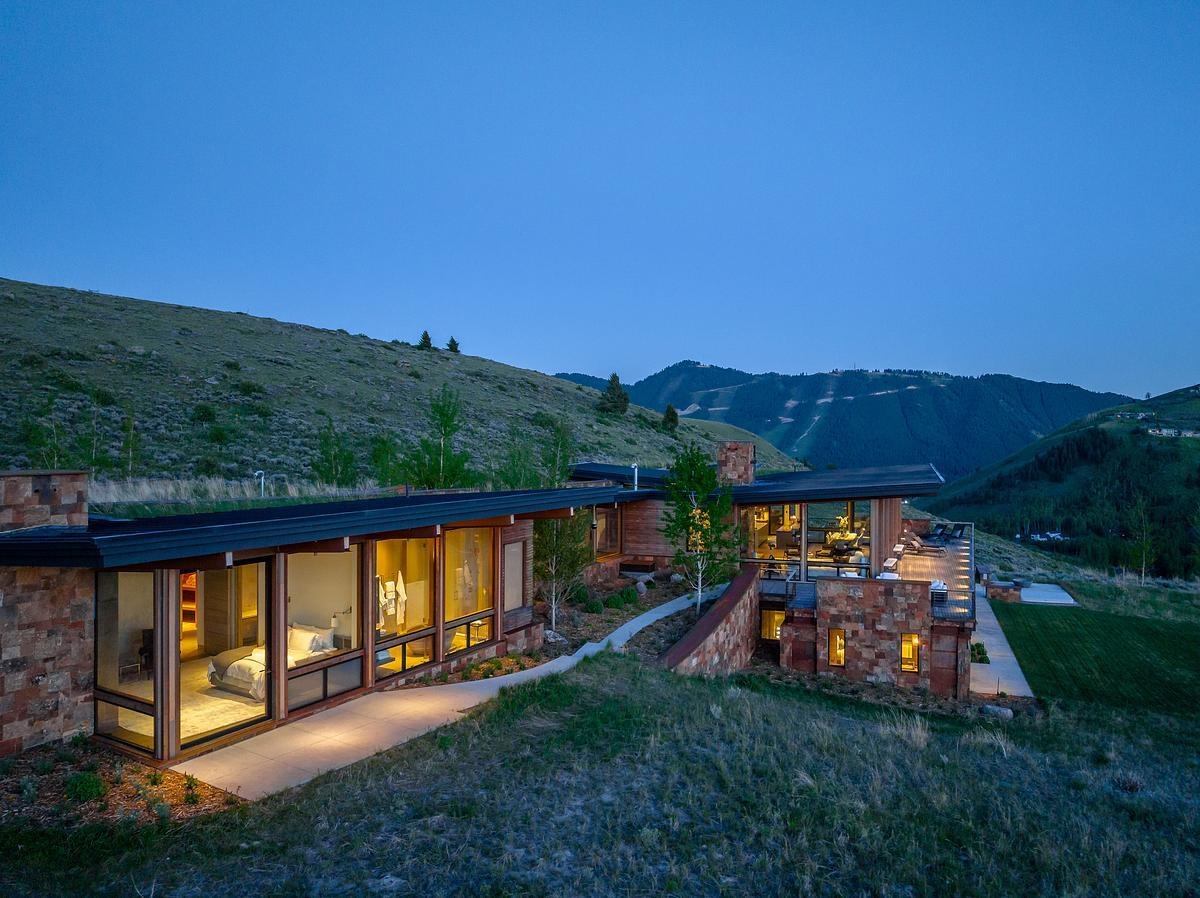 At night, the house glows softly against the hillside, its warm interior light spilling through expansive windows and casting a gentle glow onto the surrounding landscape. From a distance, it feels almost like a quiet lantern tucked into the slope.