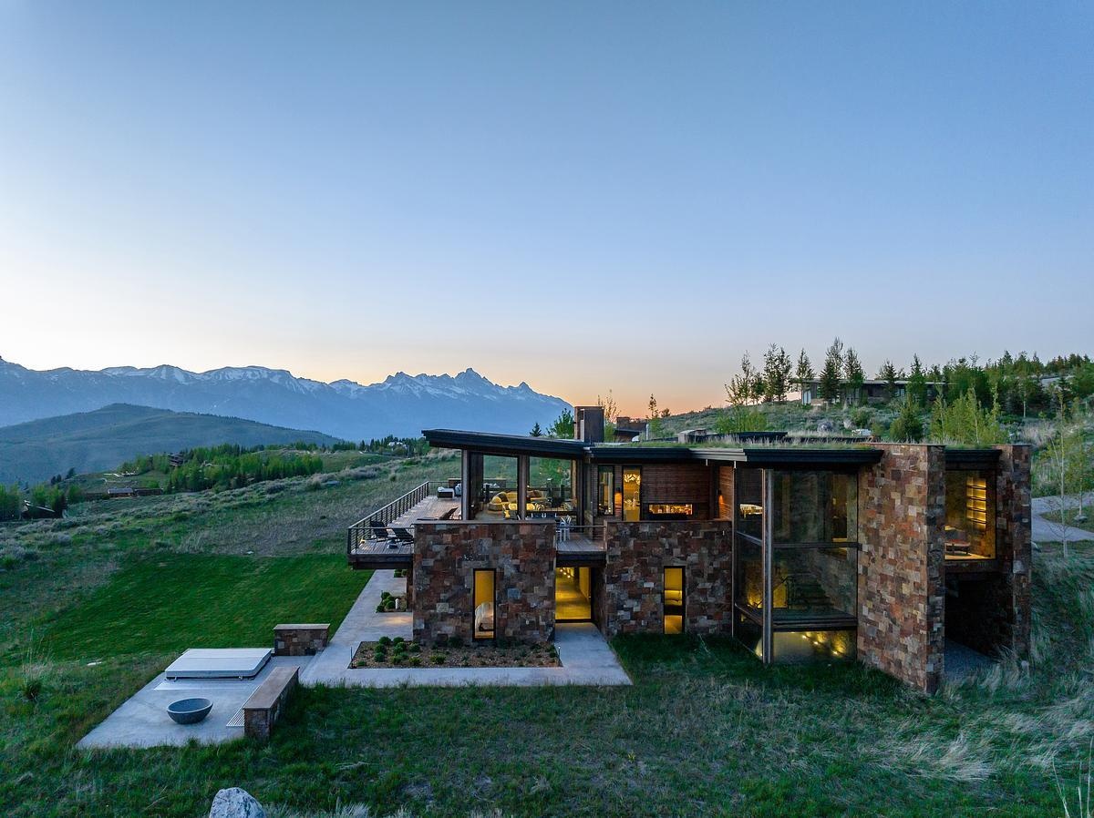 At night, the house glows softly against the hillside, its warm interior light spilling through expansive windows and casting a gentle glow onto the surrounding landscape. From a distance, it feels almost like a quiet lantern tucked into the slope.