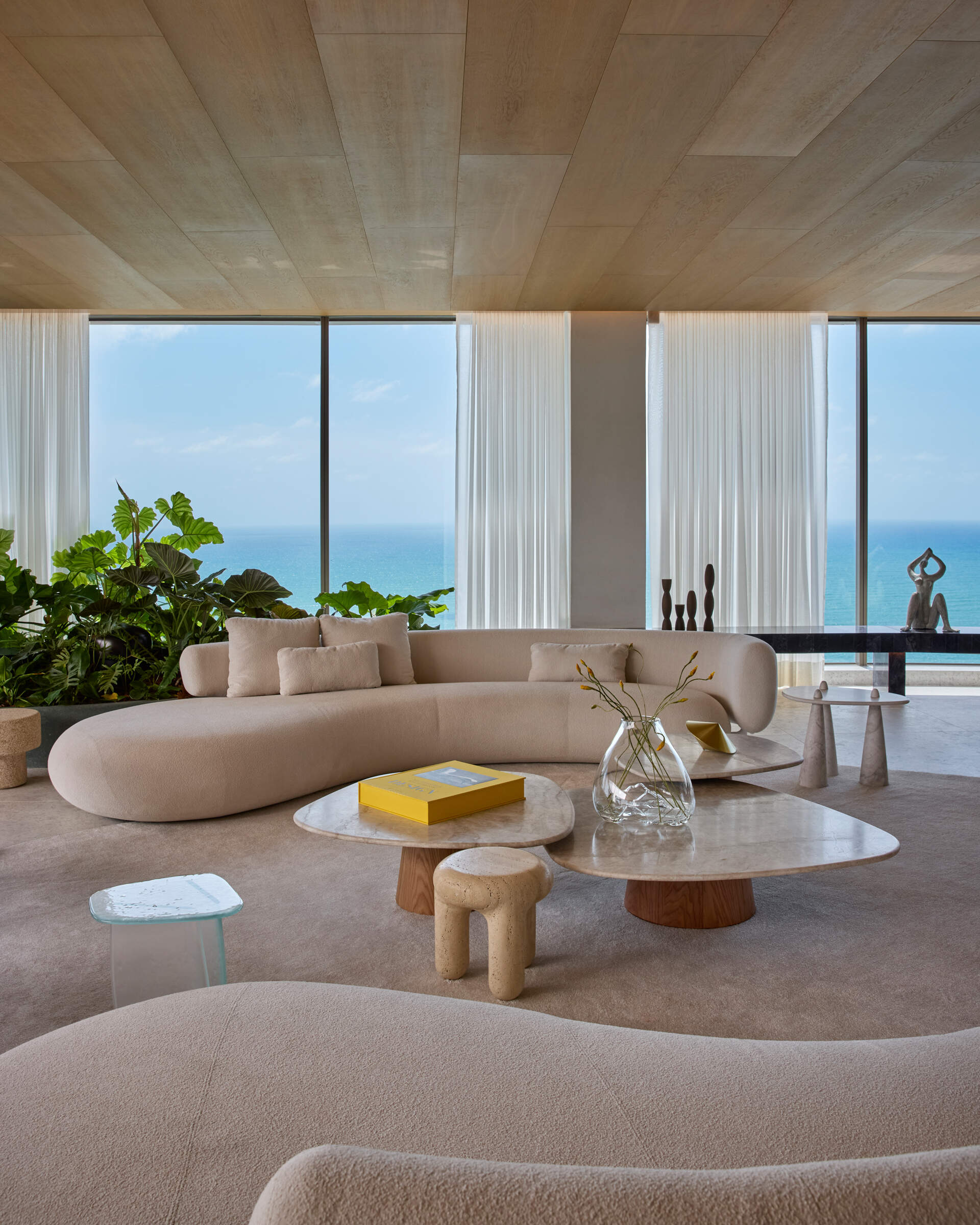 A full wall of windows frames panoramic ocean views in this Recife apartment. Neutral tones and curved furniture keep the focus on the horizon.