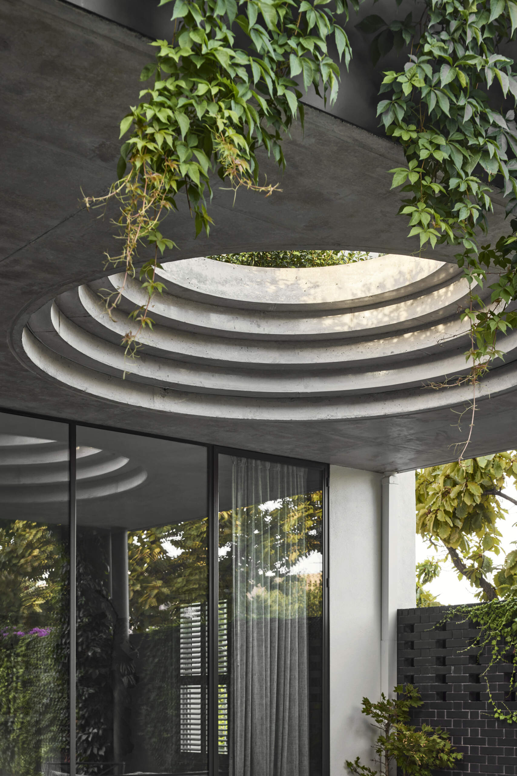 A defining feature of the rear of this remodeled home is a courtyard with a large circular cut-out overhead, a bold geometric move that invites sky views and dappled sunlight into the space below. Positioned above the outdoor dining area, the cut-out frames the moment, turning the patio into more than just a transitional space.