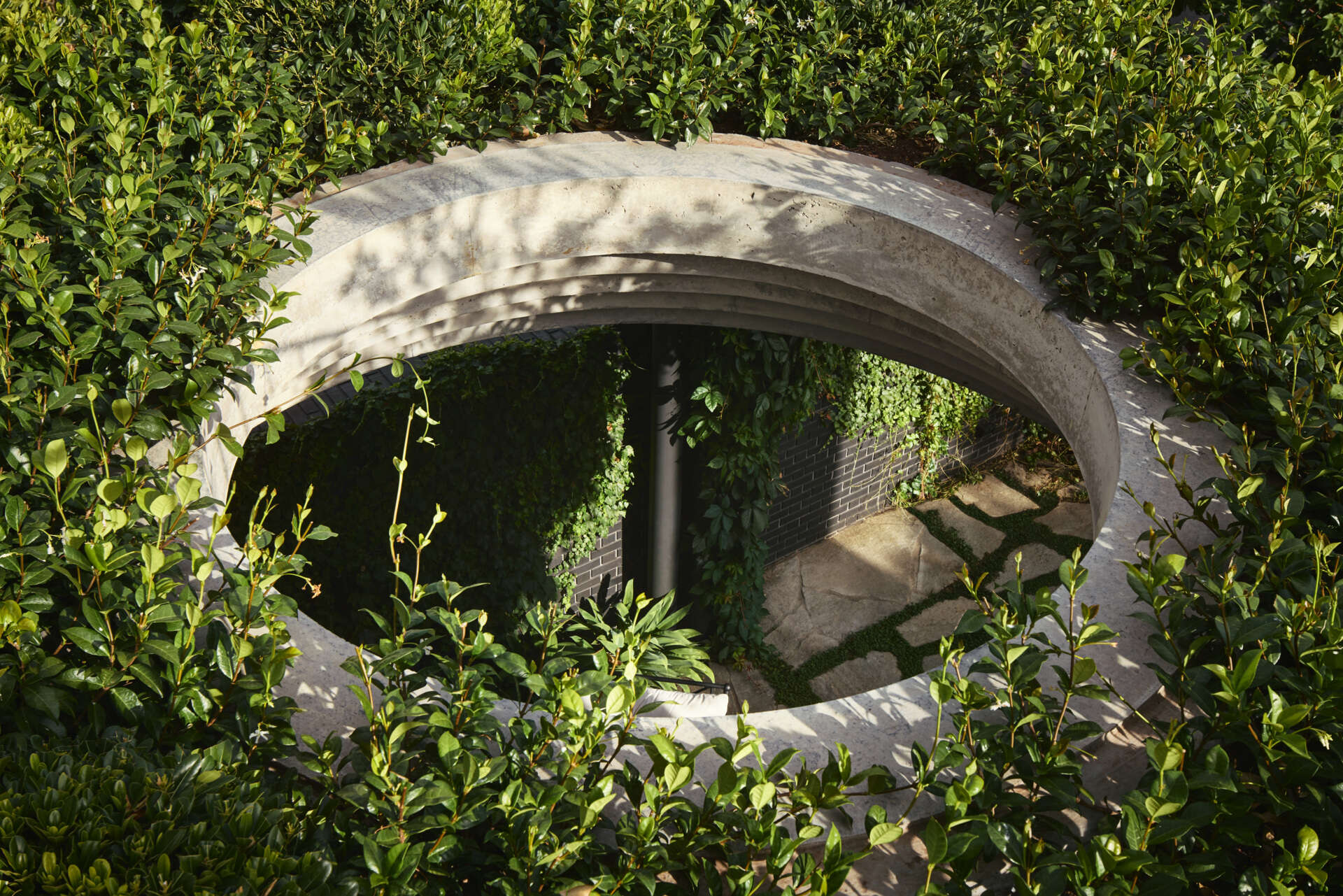 A defining feature of the rear of this remodeled home is a courtyard with a large circular cut-out overhead, a bold geometric move that invites sky views and dappled sunlight into the space below. Positioned above the outdoor dining area, the cut-out frames the moment, turning the patio into more than just a transitional space.