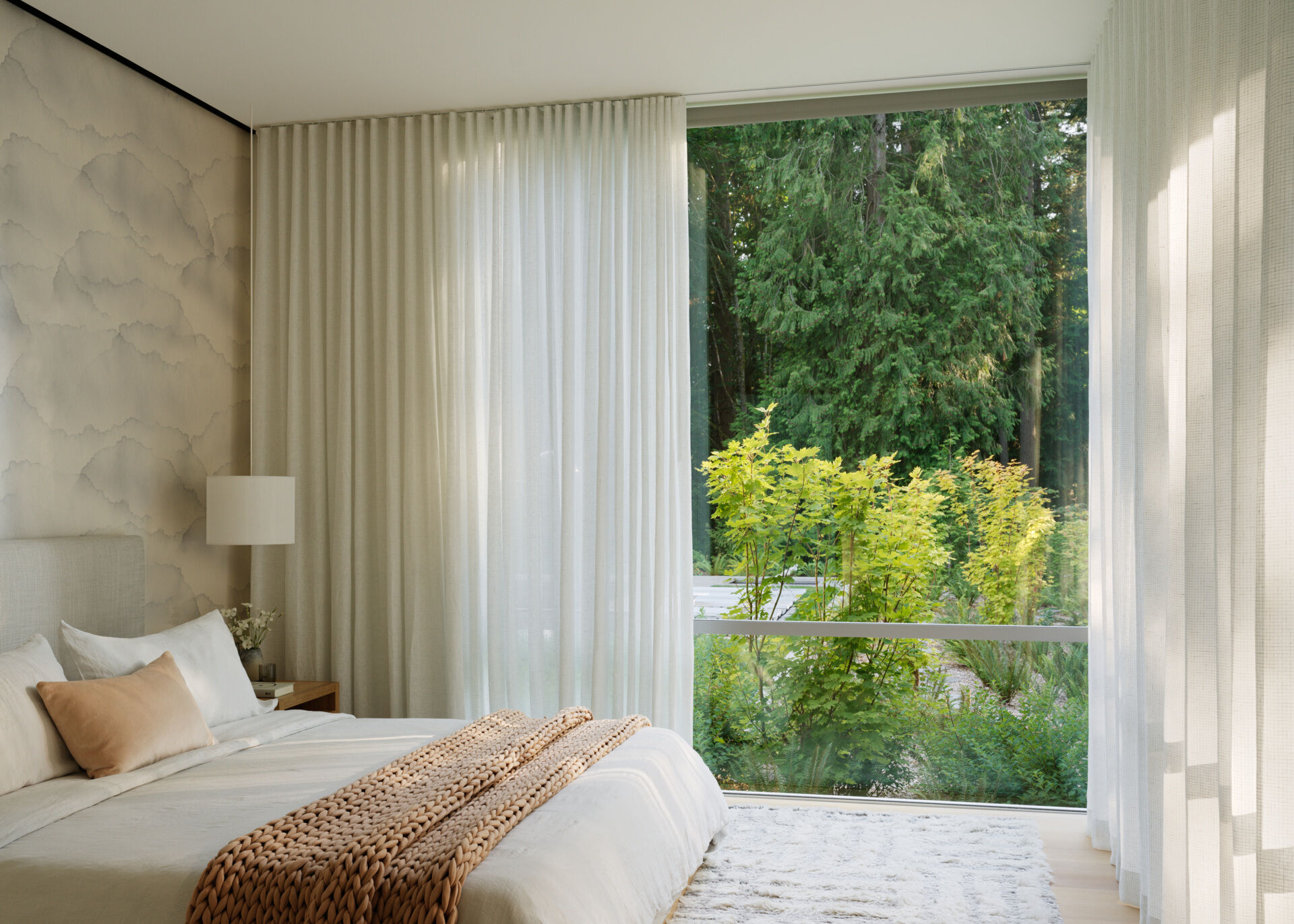 Positioned for privacy, the primary bedroom looks out onto untouched woodland. The room’s design emphasizes tranquility, neutral tones, soft textures, and high ceilings that draw the eye upward. Oversized windows let the forest into the space, creating a deeply restful retreat.