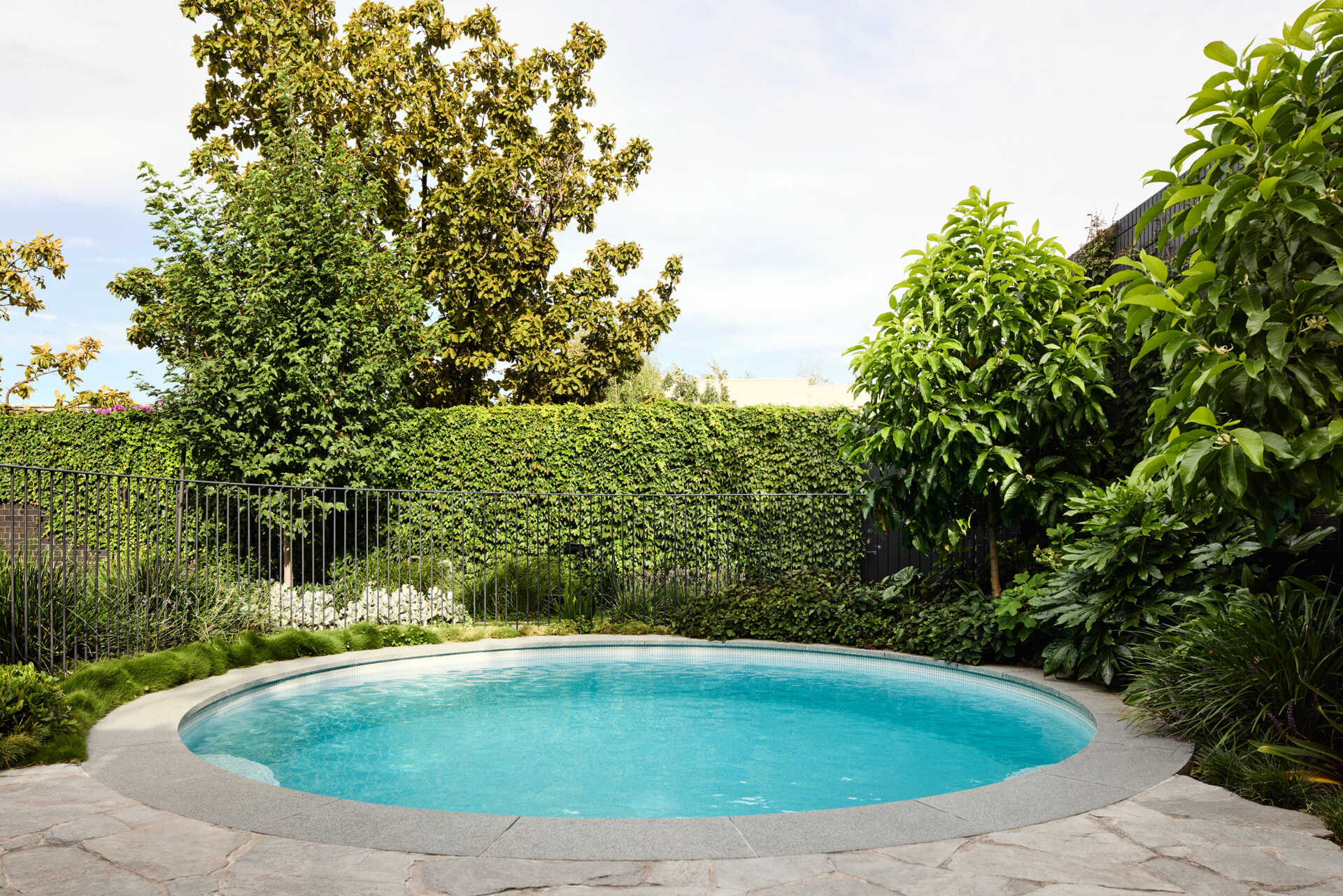 This modern landscaping plays a crucial role in defining the sanctuary-like atmosphere. With a round swimming pool, outdoor fireplace, strategic planting, and thoughtful layering, the outdoor spaces offer both privacy from the street and a lush backdrop for daily life.