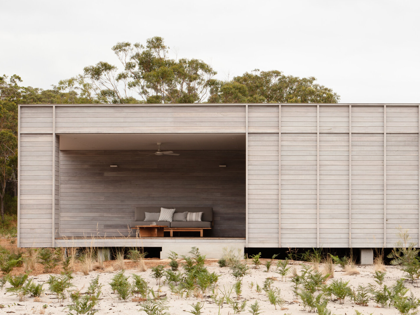 The home’s form is simple and familiar, yet subtly redefined. A generously scaled verandah anchors the dwelling and extends its living space outward, functioning more like an outdoor room than a traditional porch. This shaded threshold becomes a true living zone, equally suited to quiet mornings or social evenings, and acts as a natural bridge between the home’s interior and the landscape beyond.